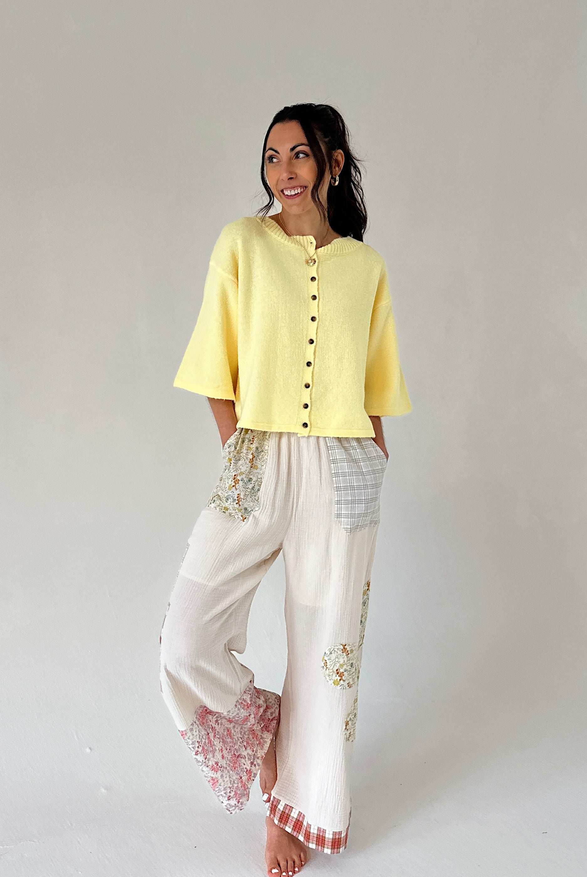 Woman wearing a yellow top and white pants with lace details on a plain background
