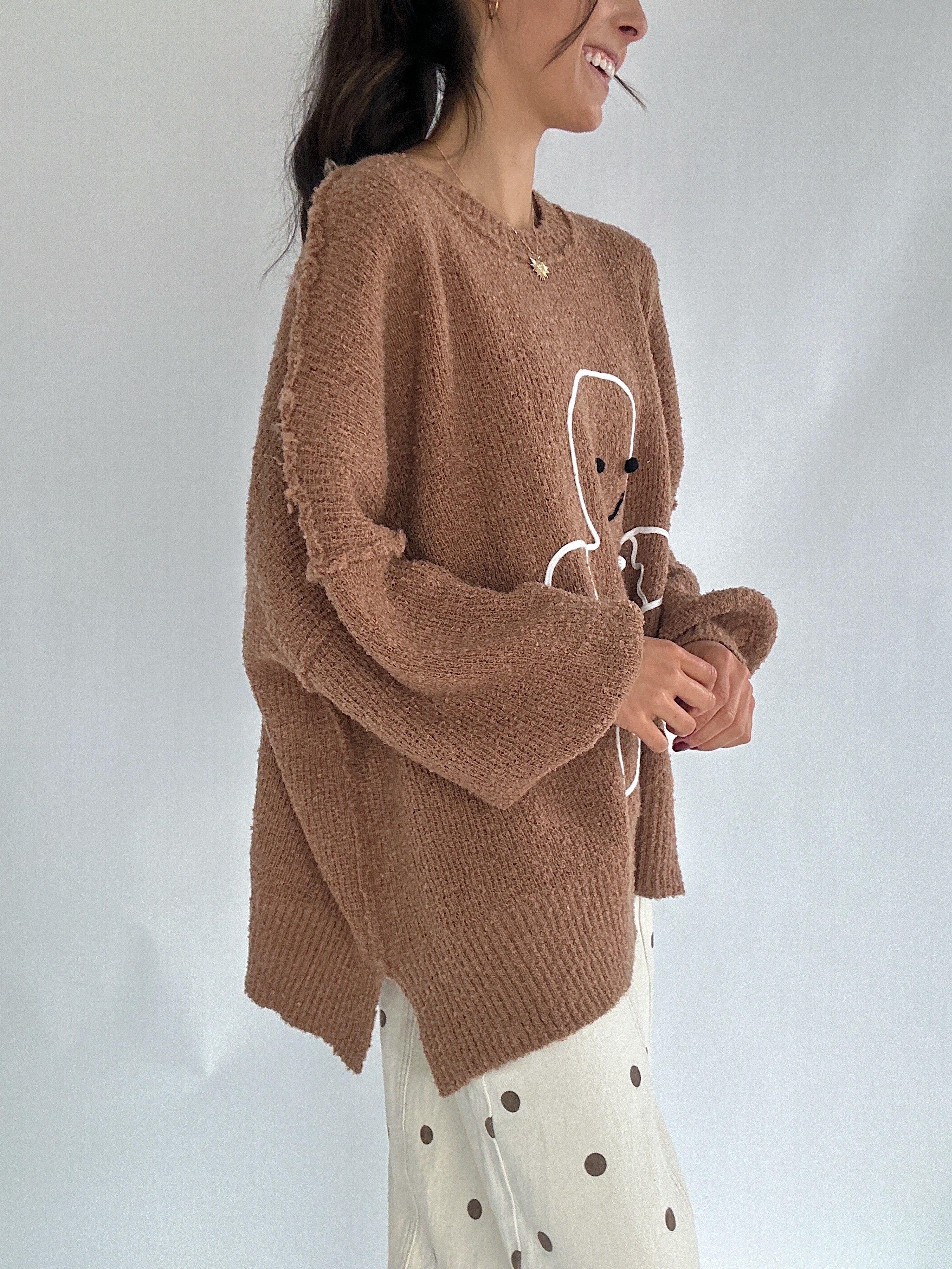 Person wearing a brown sweater with a gingerbread man design on a plain background side view