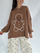 Person wearing a brown sweater with a gingerbread man design on a plain background and polka dot pants