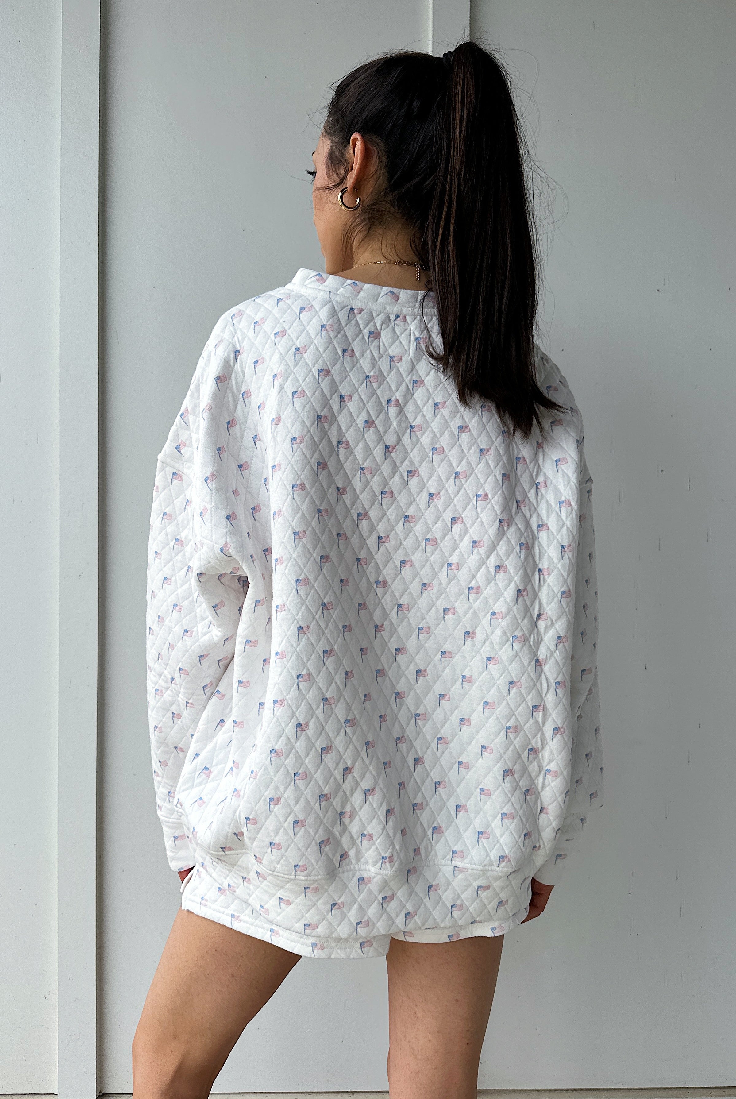Person wearing a white quilted flag patterned sweatshirt against a plain background