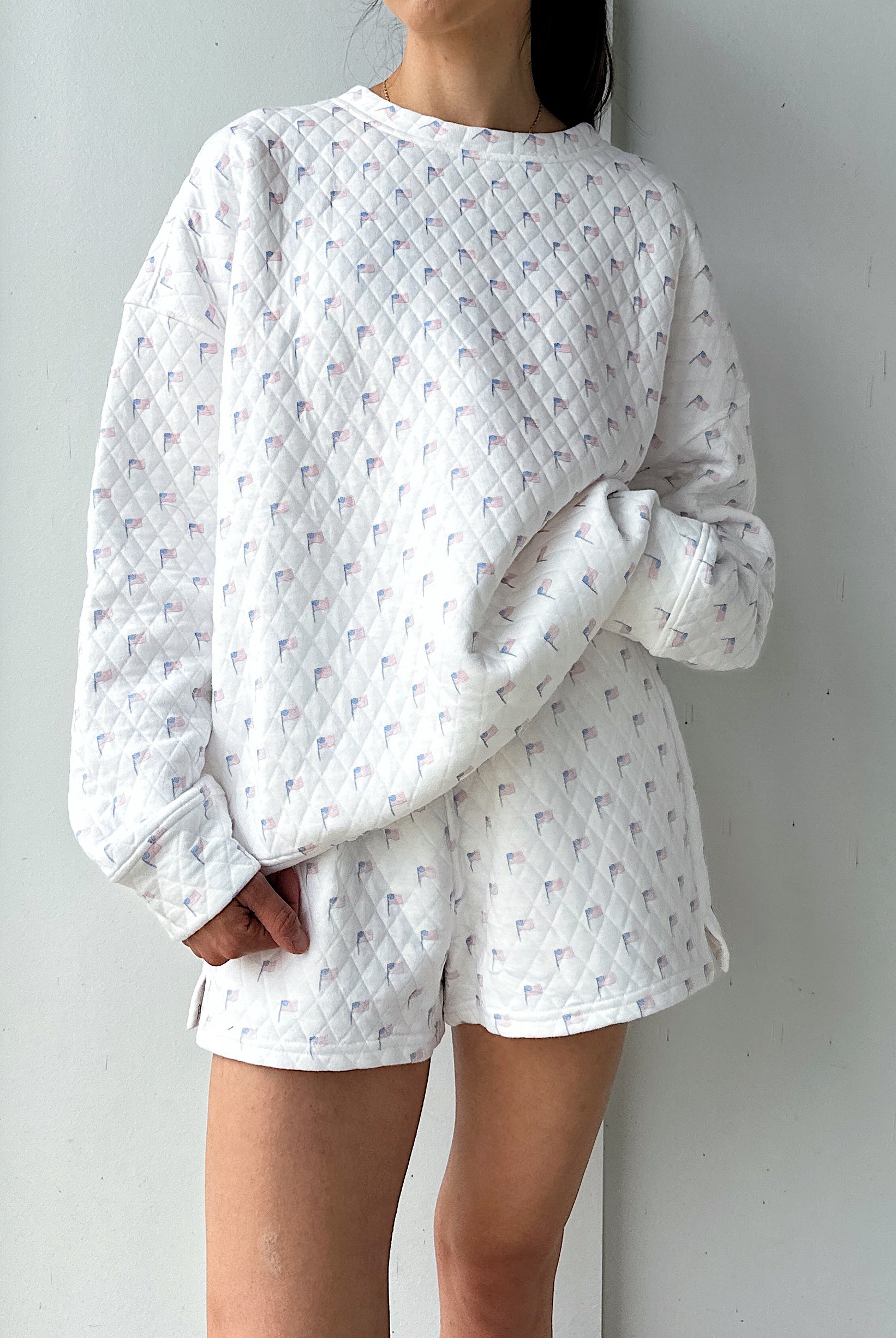 Person wearing a white quilted flag sweatshirt against a plain background