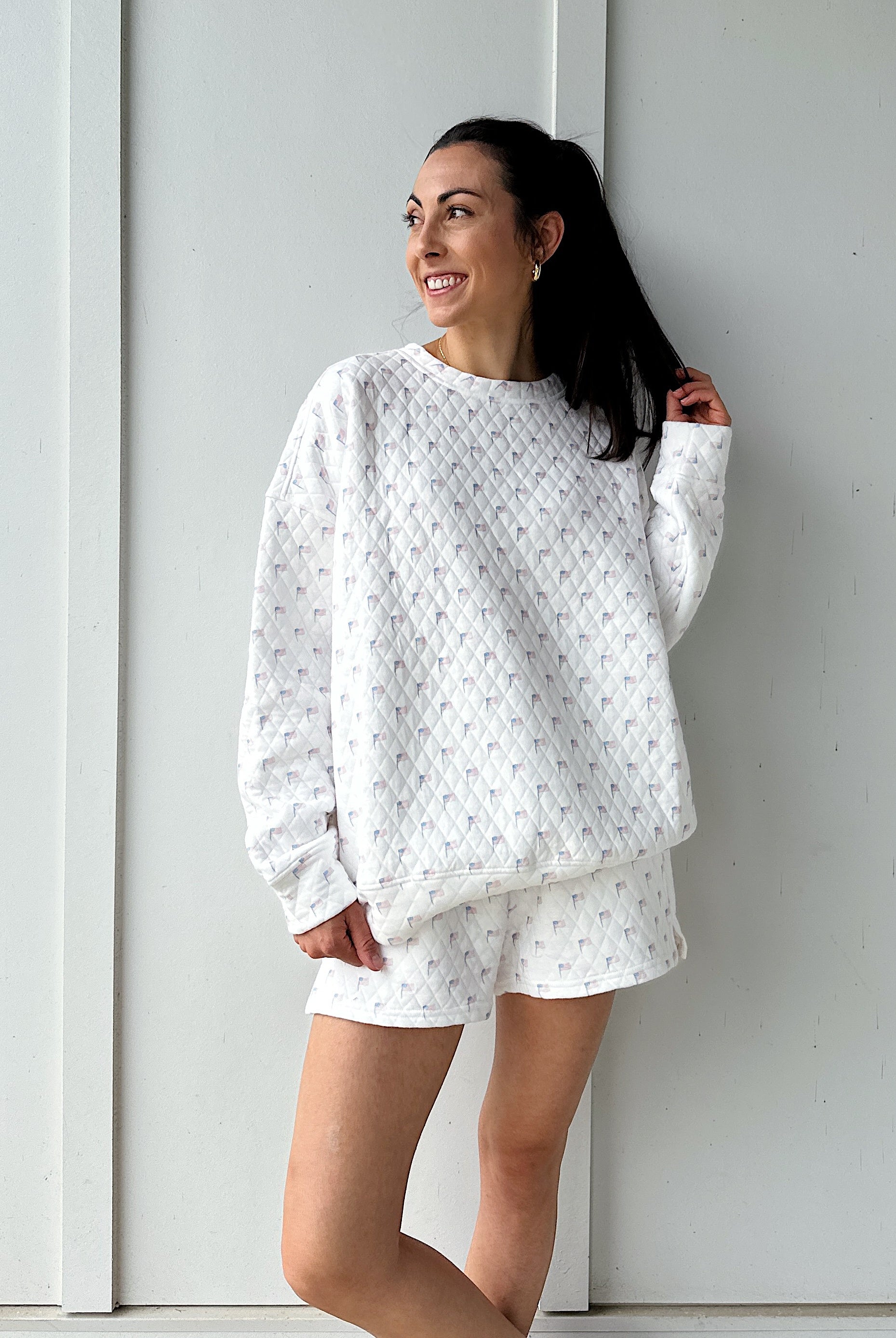 Woman wearing a white quilted flag patterned sweatshirt against a plain background