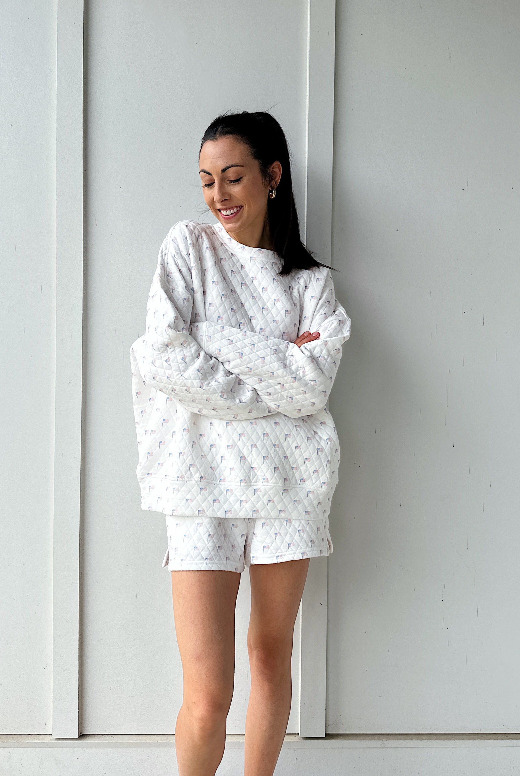 Woman wearing a white quilted flag patterned outfit standing against a white wall.