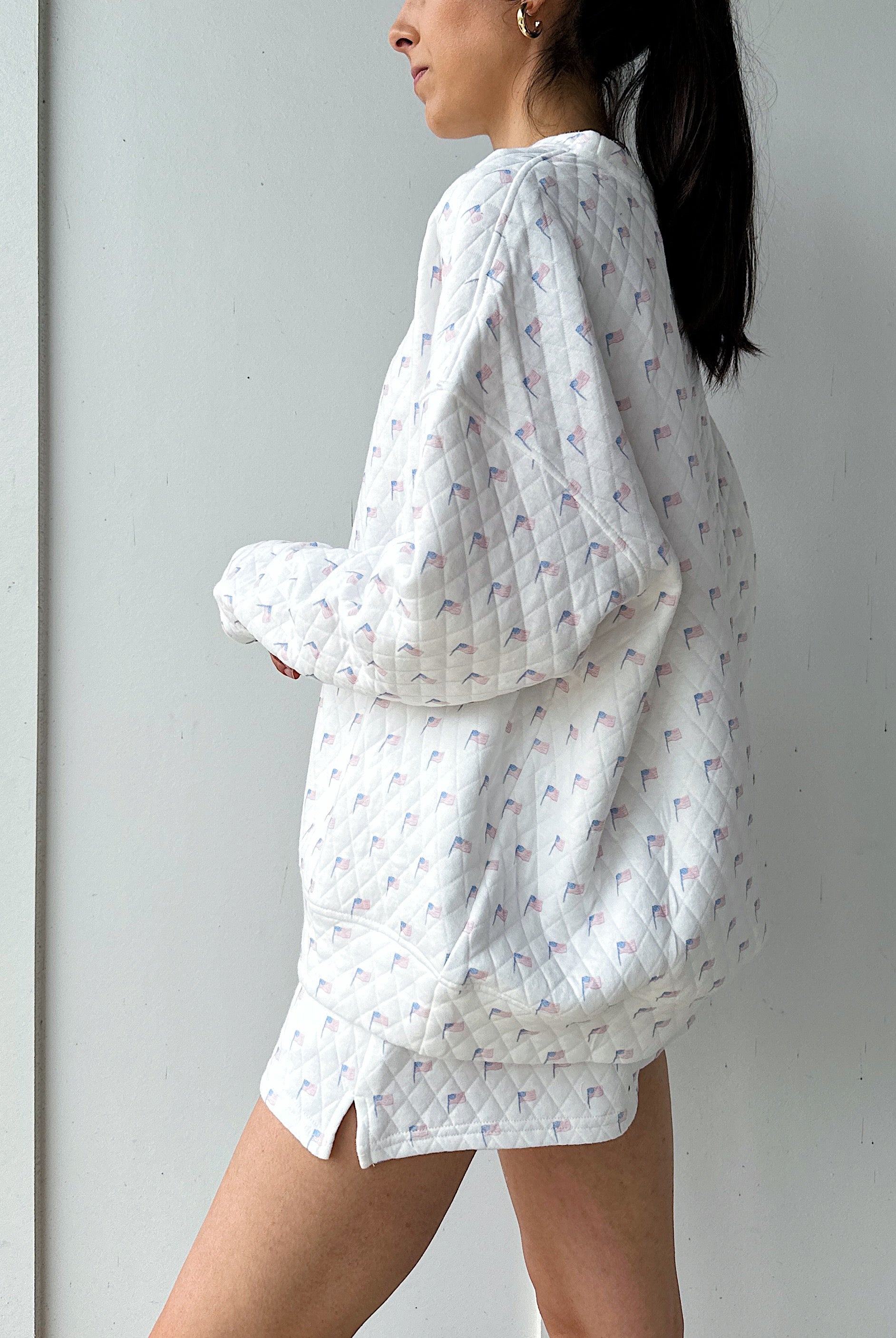 Woman wearing a white quilted flag patterned sweatshirt against a plain background