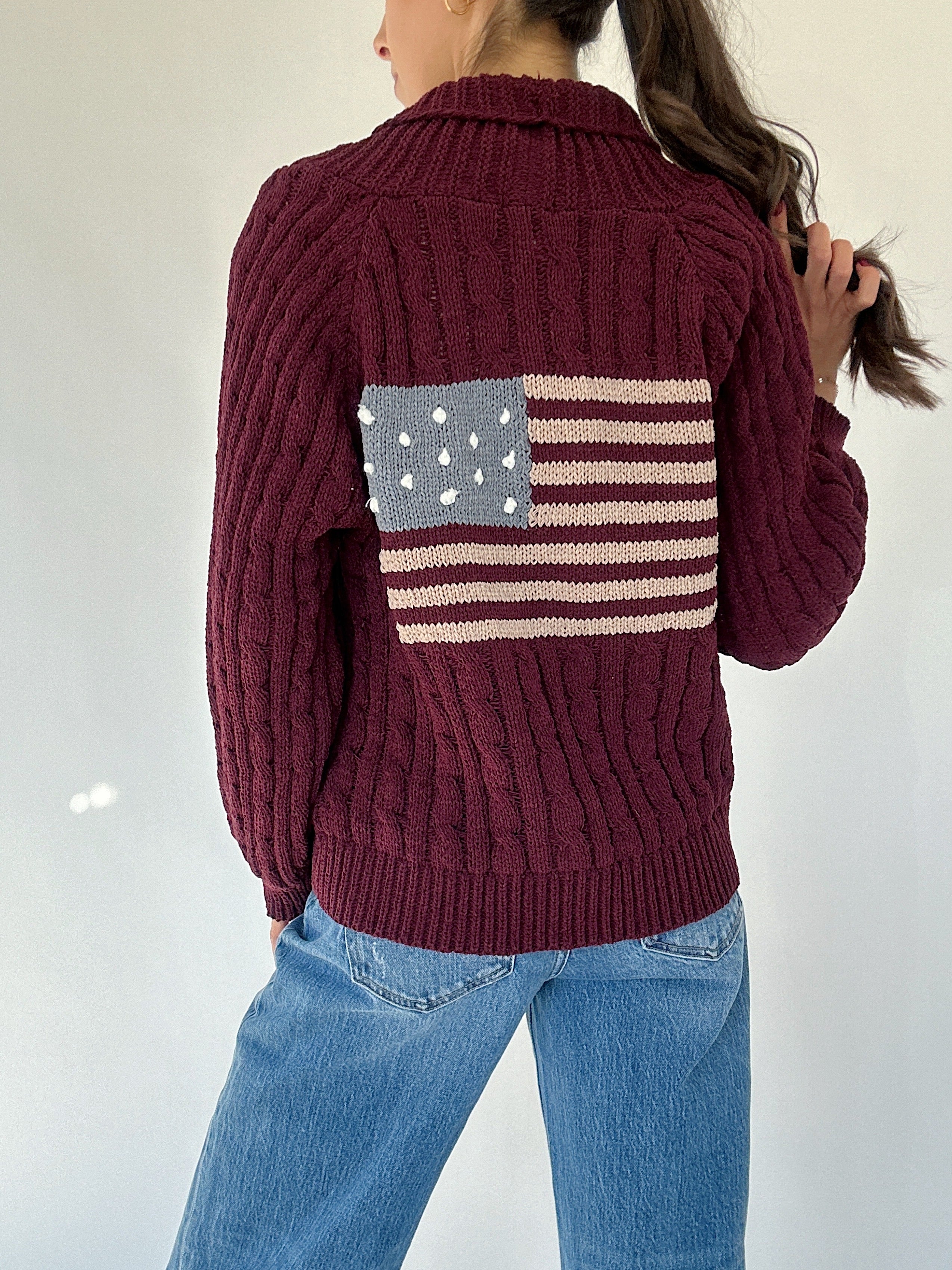 Person wearing a chenille maroon sweater with an American flag design on the back against a white background