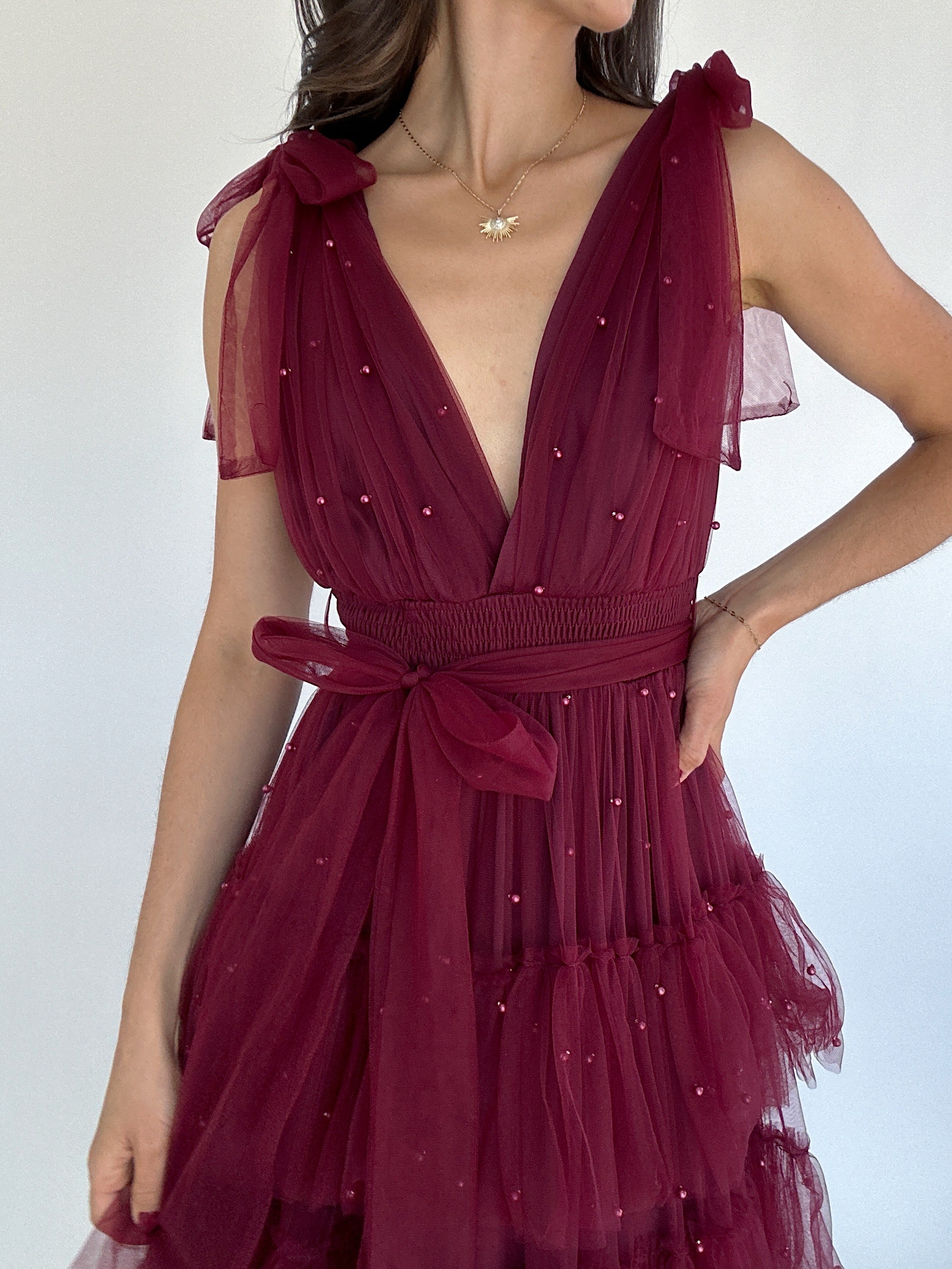 Maroon dress with pearl embellishments on a plain background to show deep v neckline and sash waist and tie straps