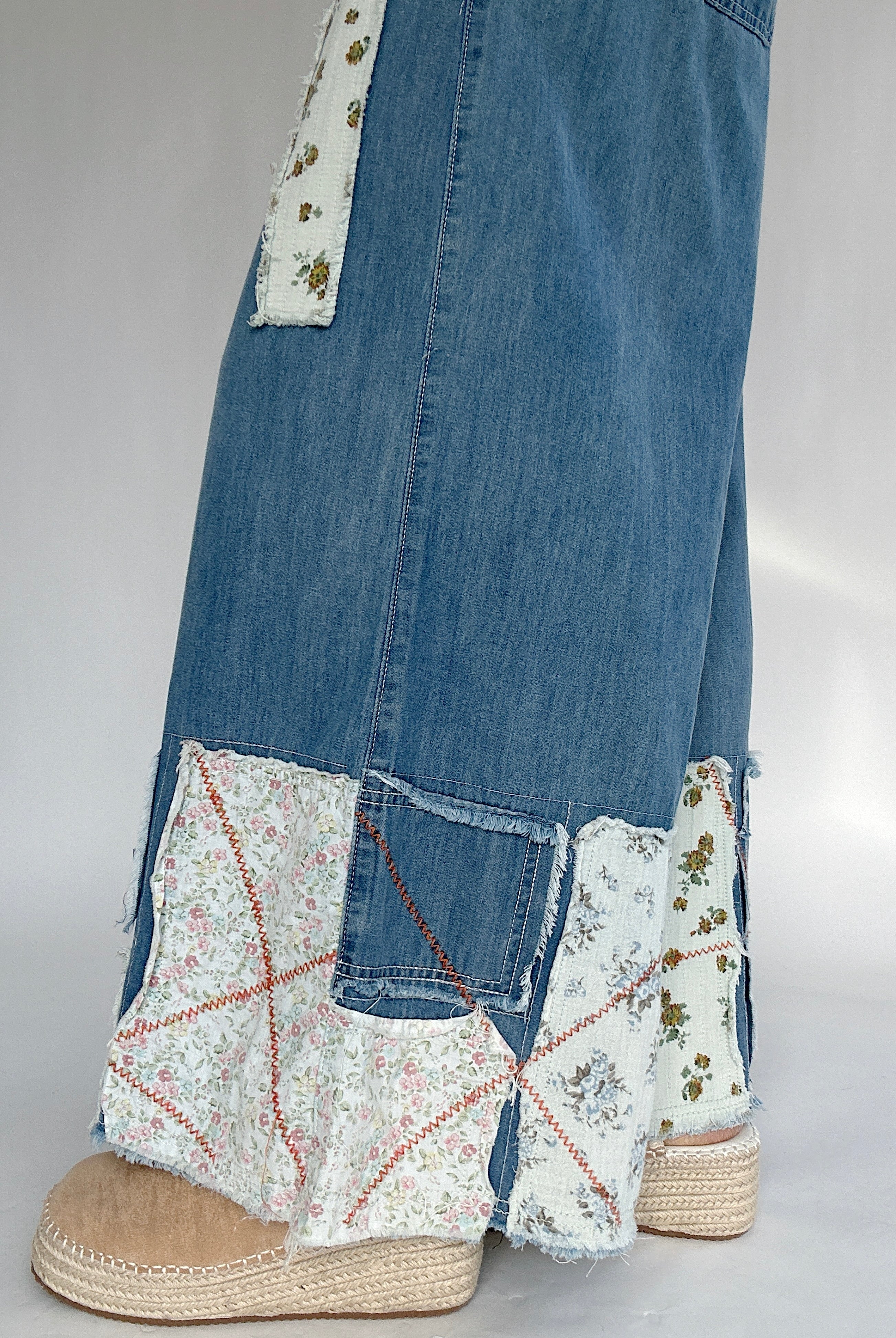 Denim pants with floral patchwork and espadrille clogs on a white gray background to show patchwork details