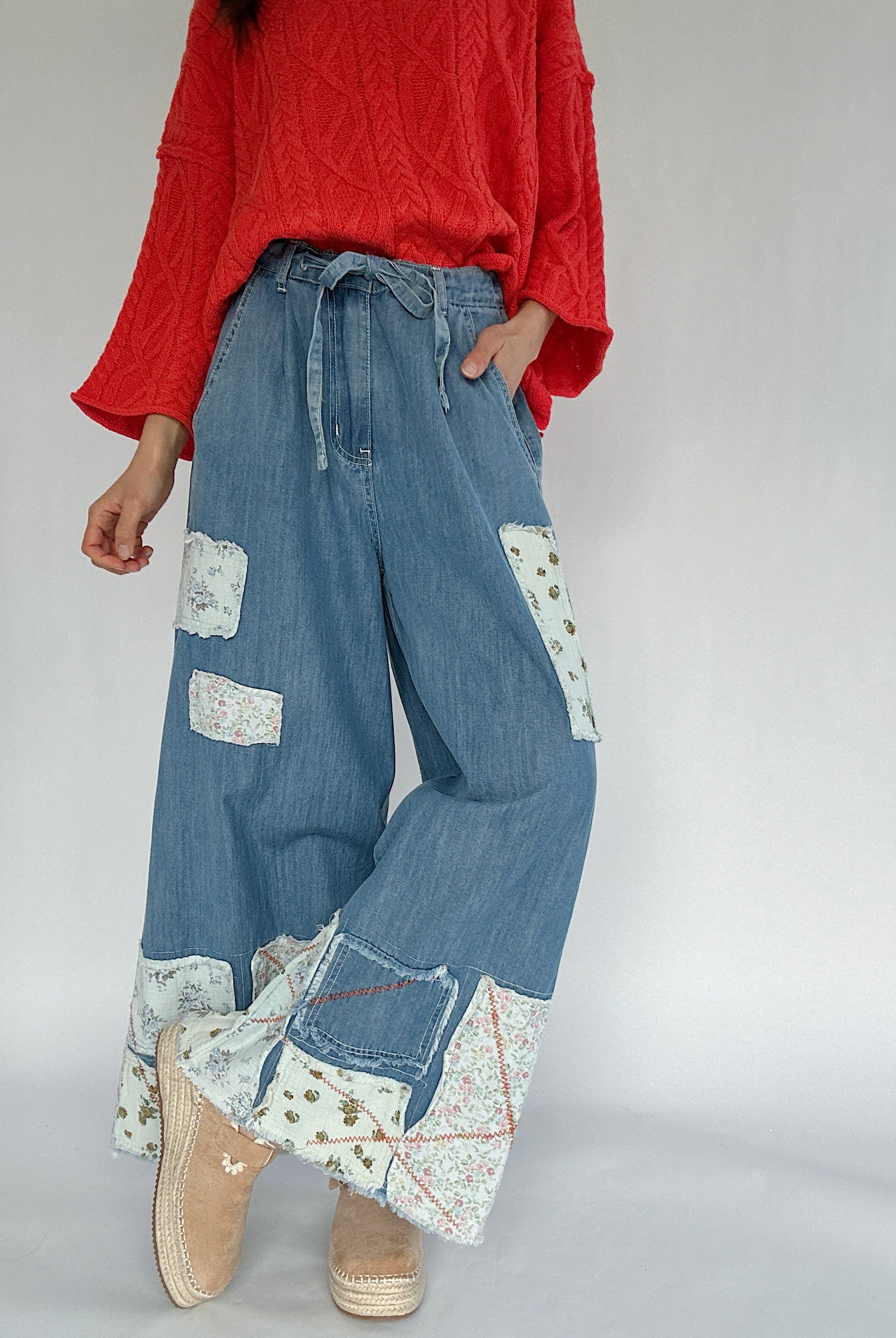 Person wearing a bright coral sweater and blue patchwork wide leg jeans on a plain background