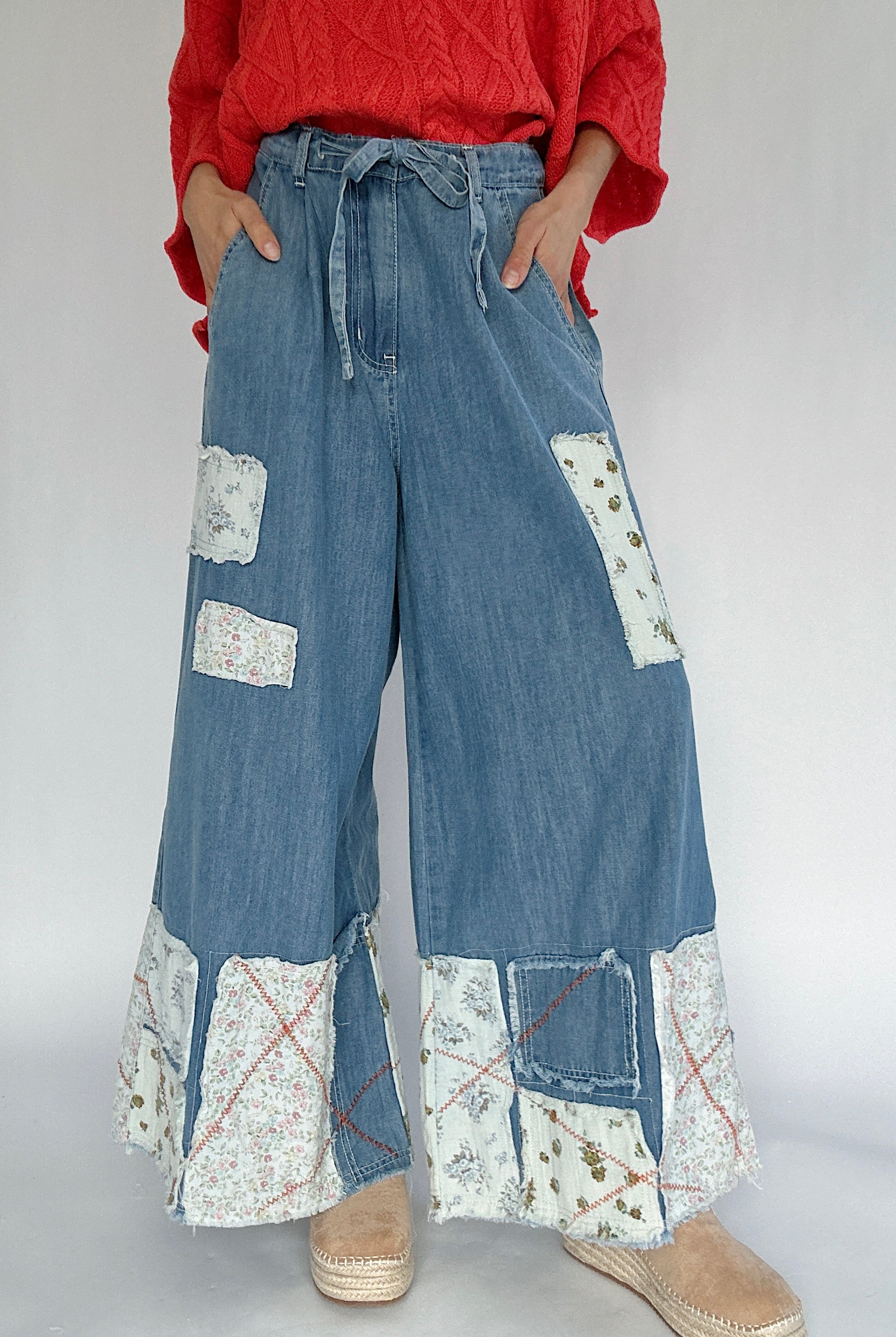 Person wearing blue denim wide leg pants with patchwork details and a bright coral sweater.
