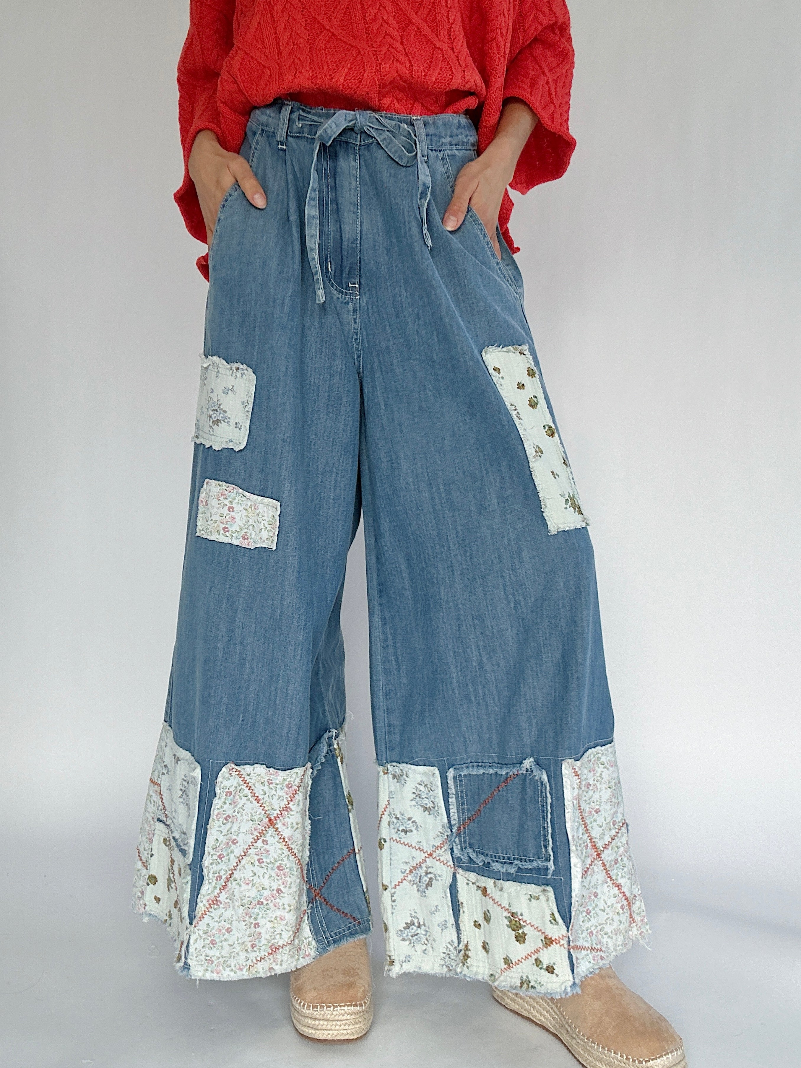 Person wearing blue denim wide leg pants with patchwork details and a bright coral sweater.