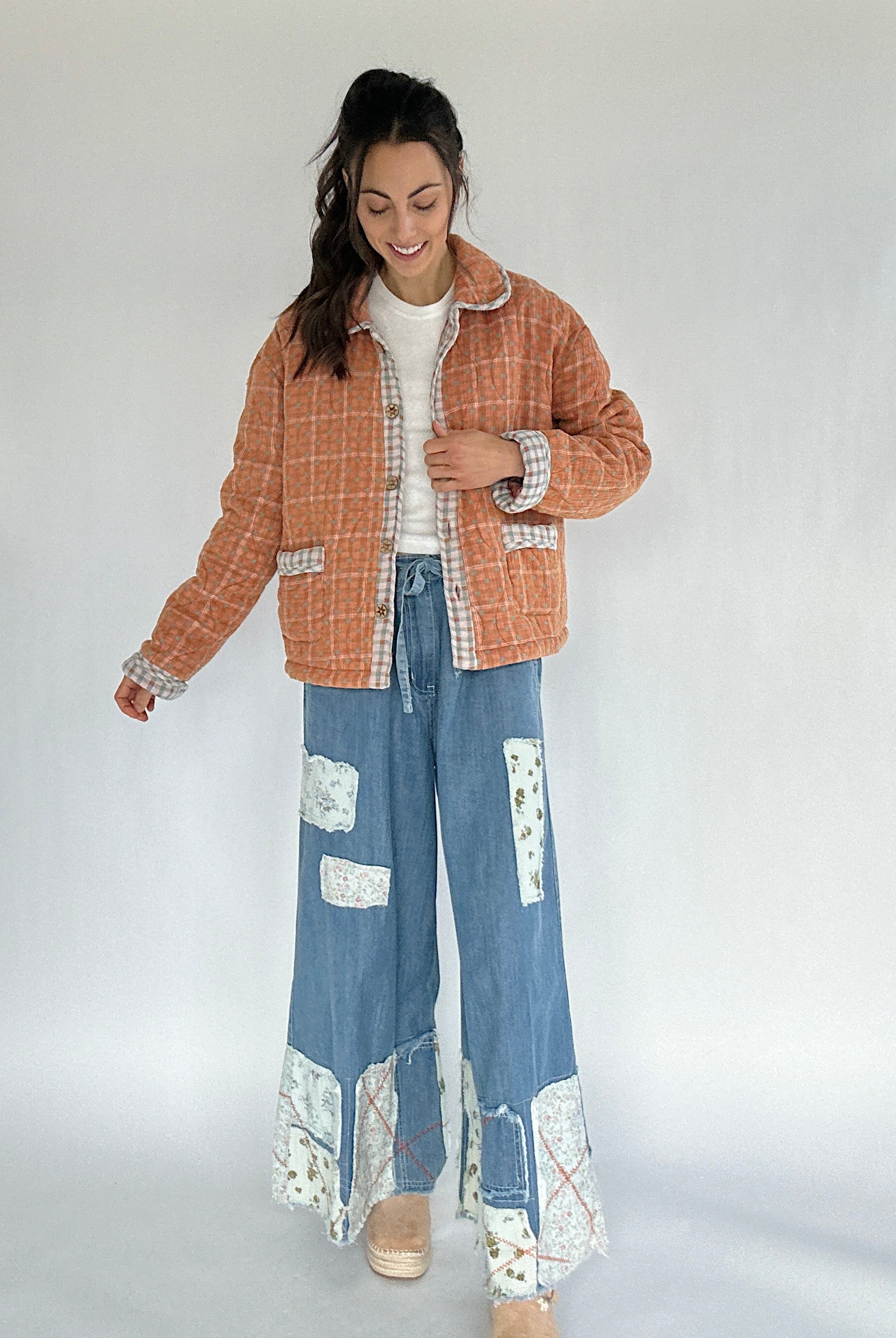 Woman wearing a checkered jacket and denim pants with floral patterns on a white background