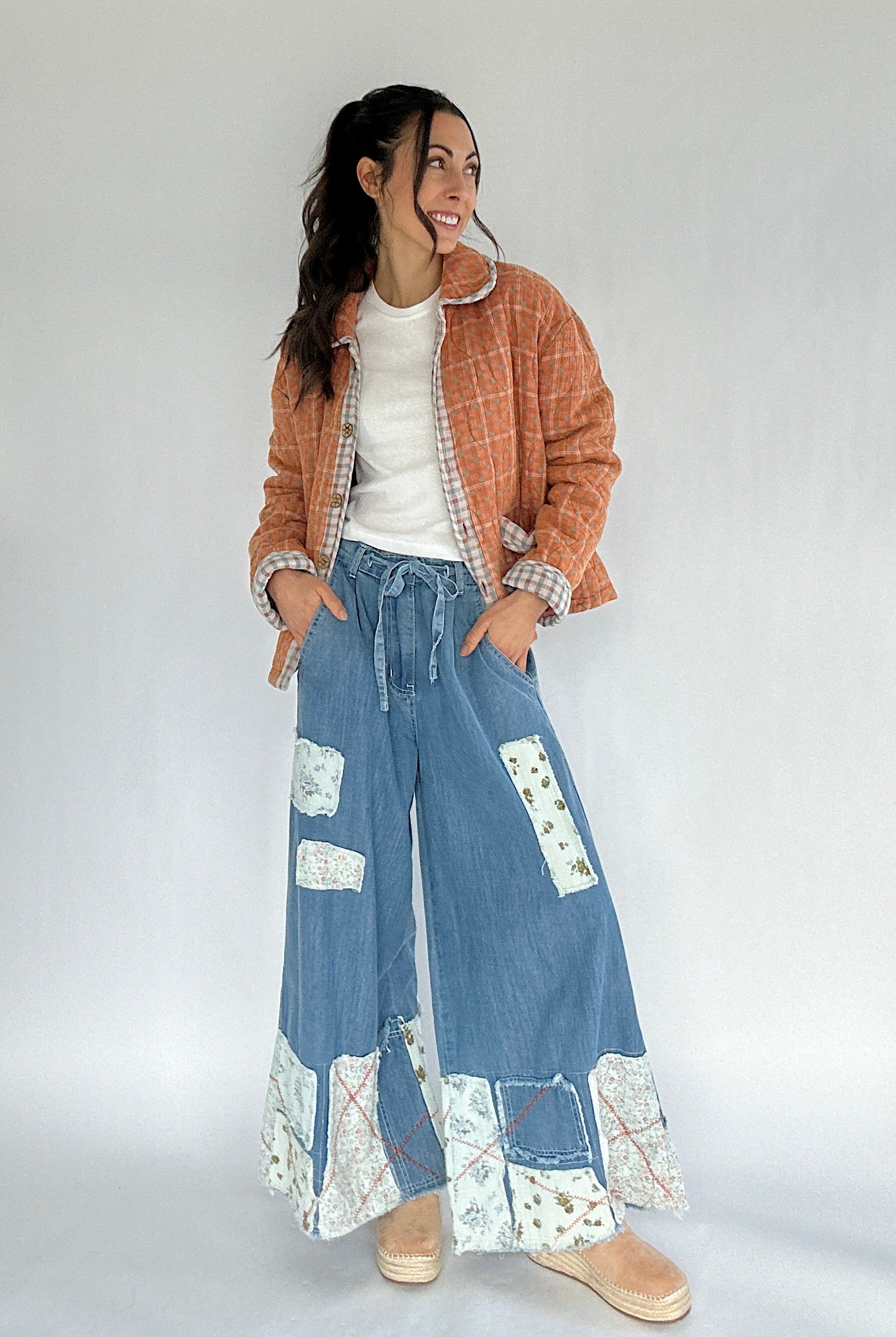 Woman wearing a plaid jacket, white shirt, and blue patchwork pants on a plain background