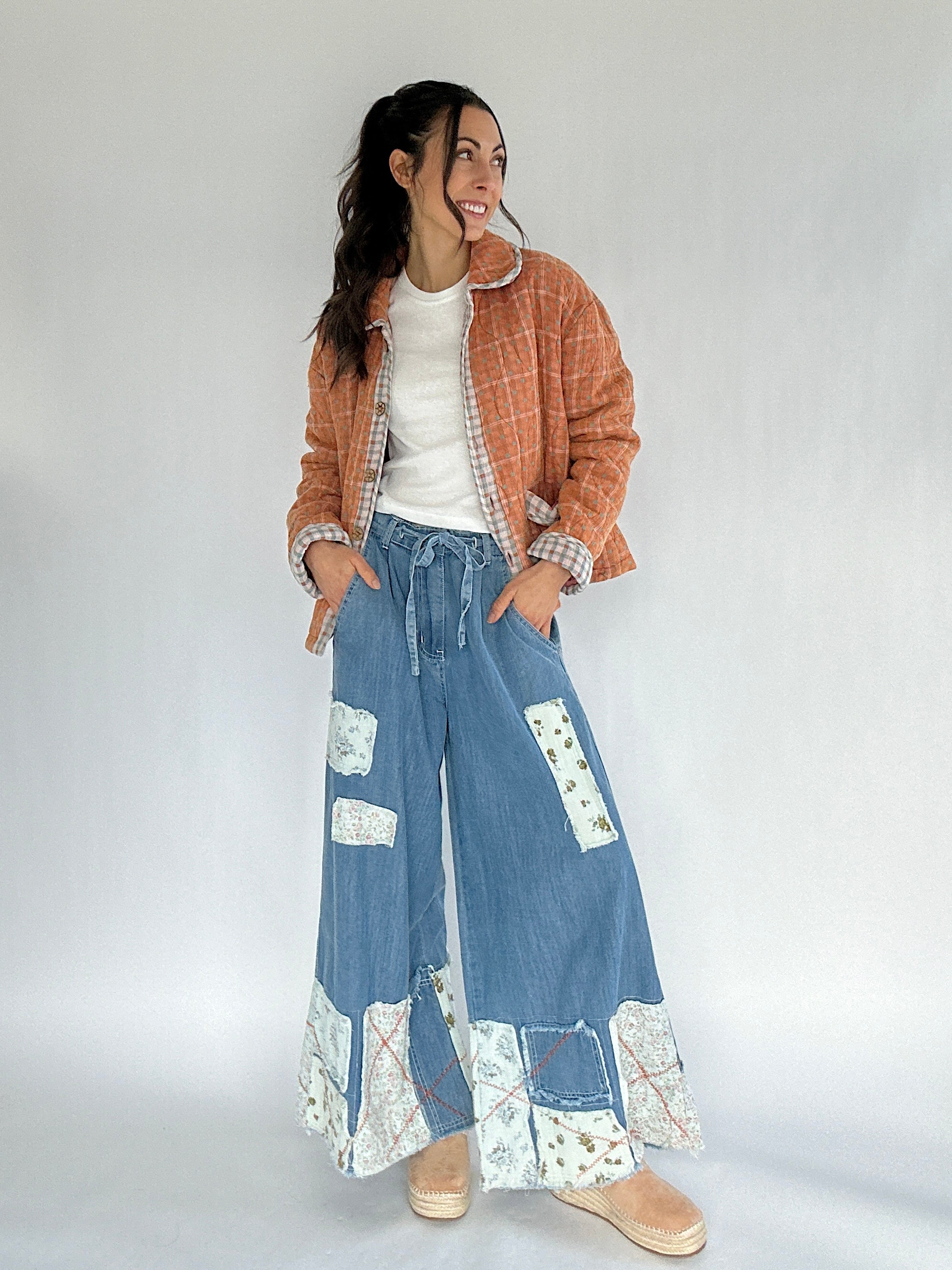 Woman wearing a plaid jacket, white shirt, and blue patchwork pants on a plain background