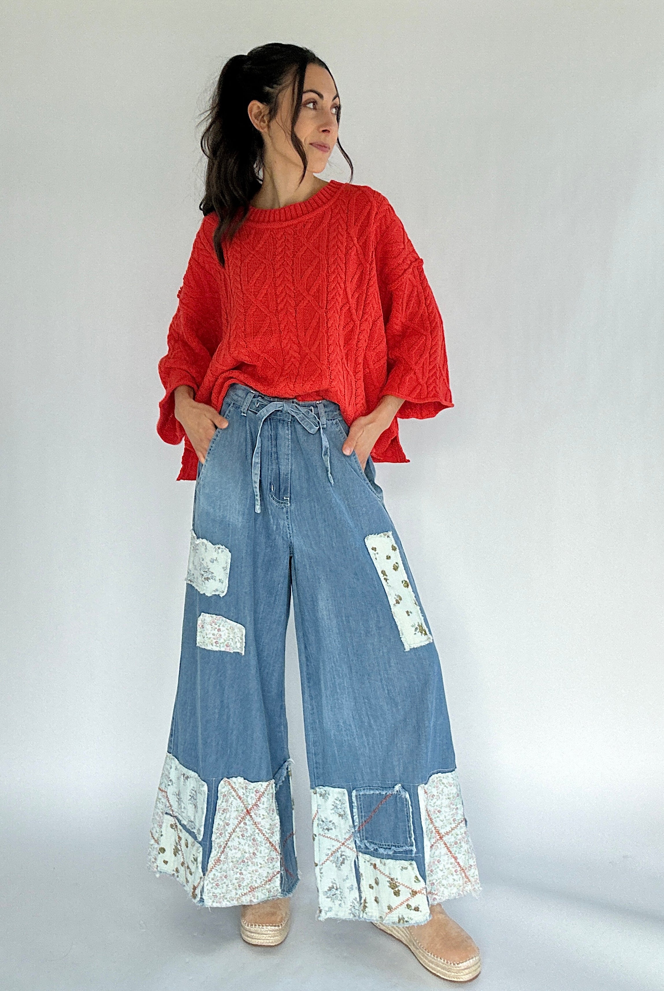 Woman wearing a coral sweater and blue patchwork wide leg pants on a white background