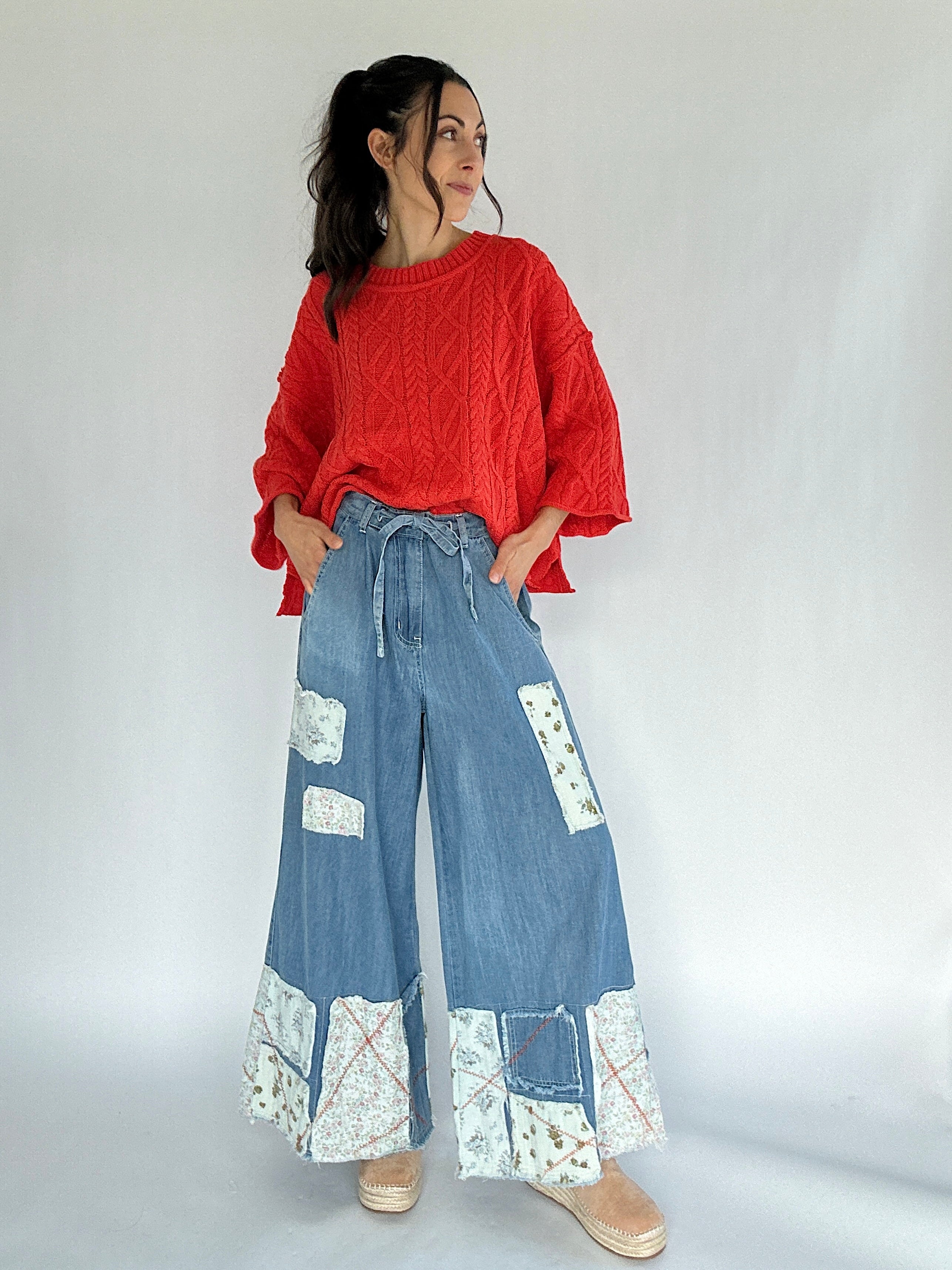 Woman wearing a coral sweater and blue patchwork wide leg pants on a white background