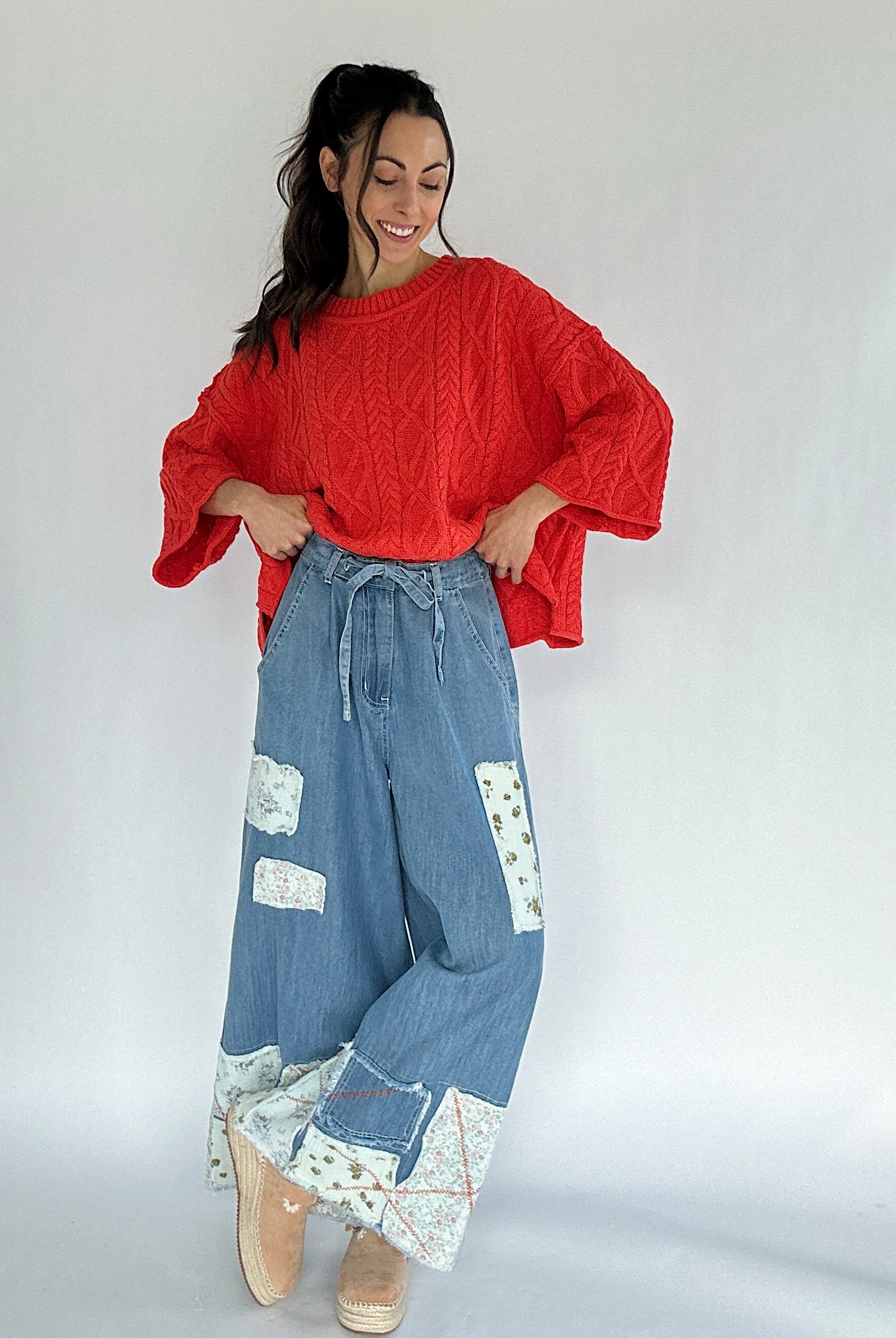 Woman wearing a bright coral sweater and blue patchwork pants on a white background