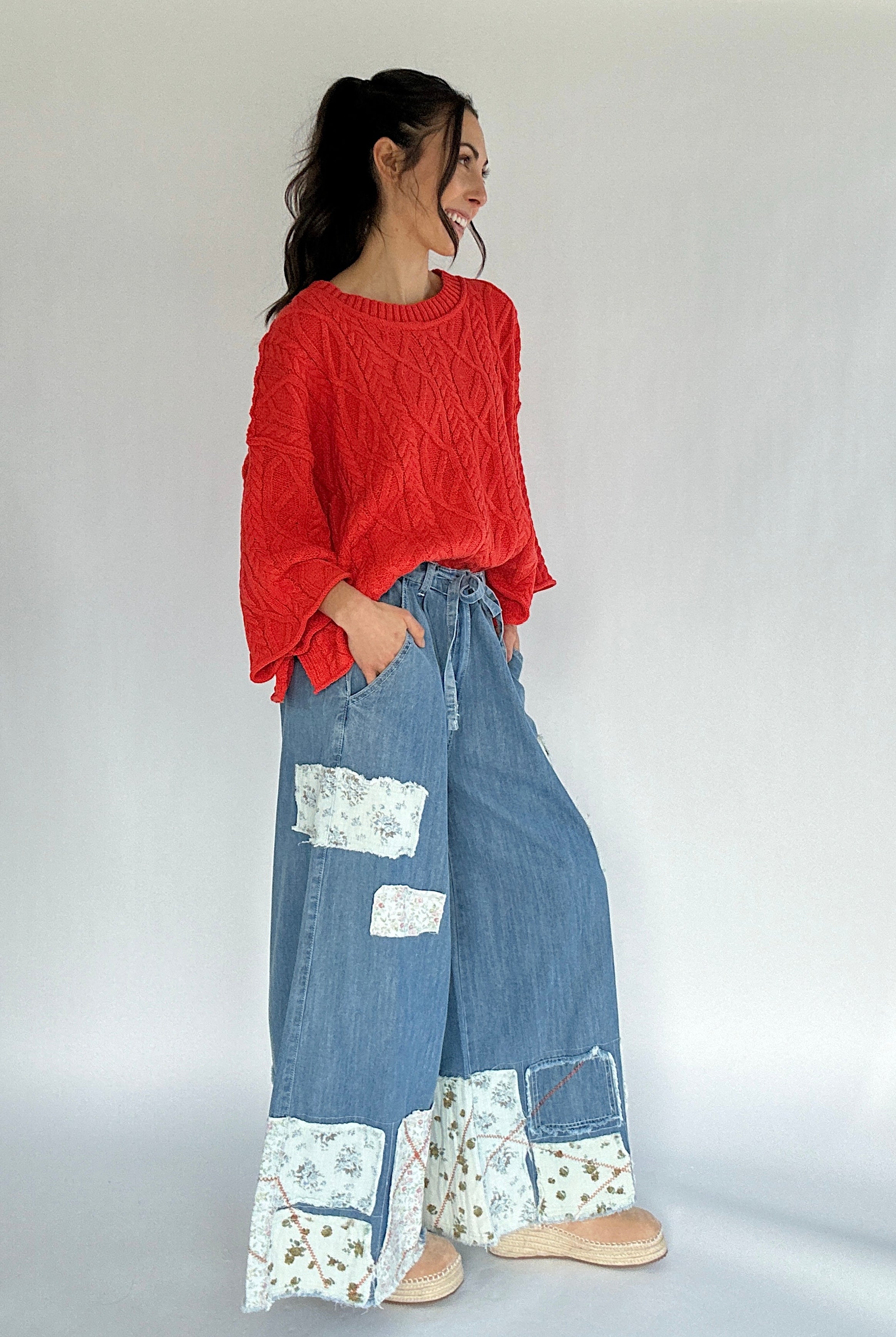 Woman wearing a bright coral sweater and blue patchwork pants on a white background