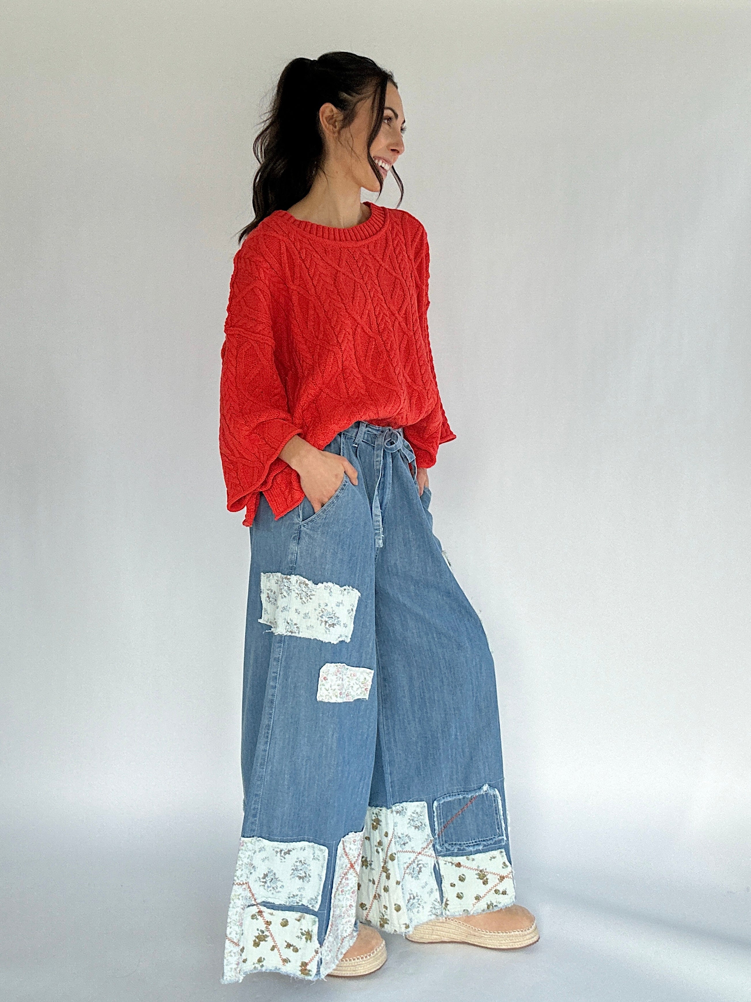 Woman wearing a bright coral sweater and blue patchwork pants on a white background