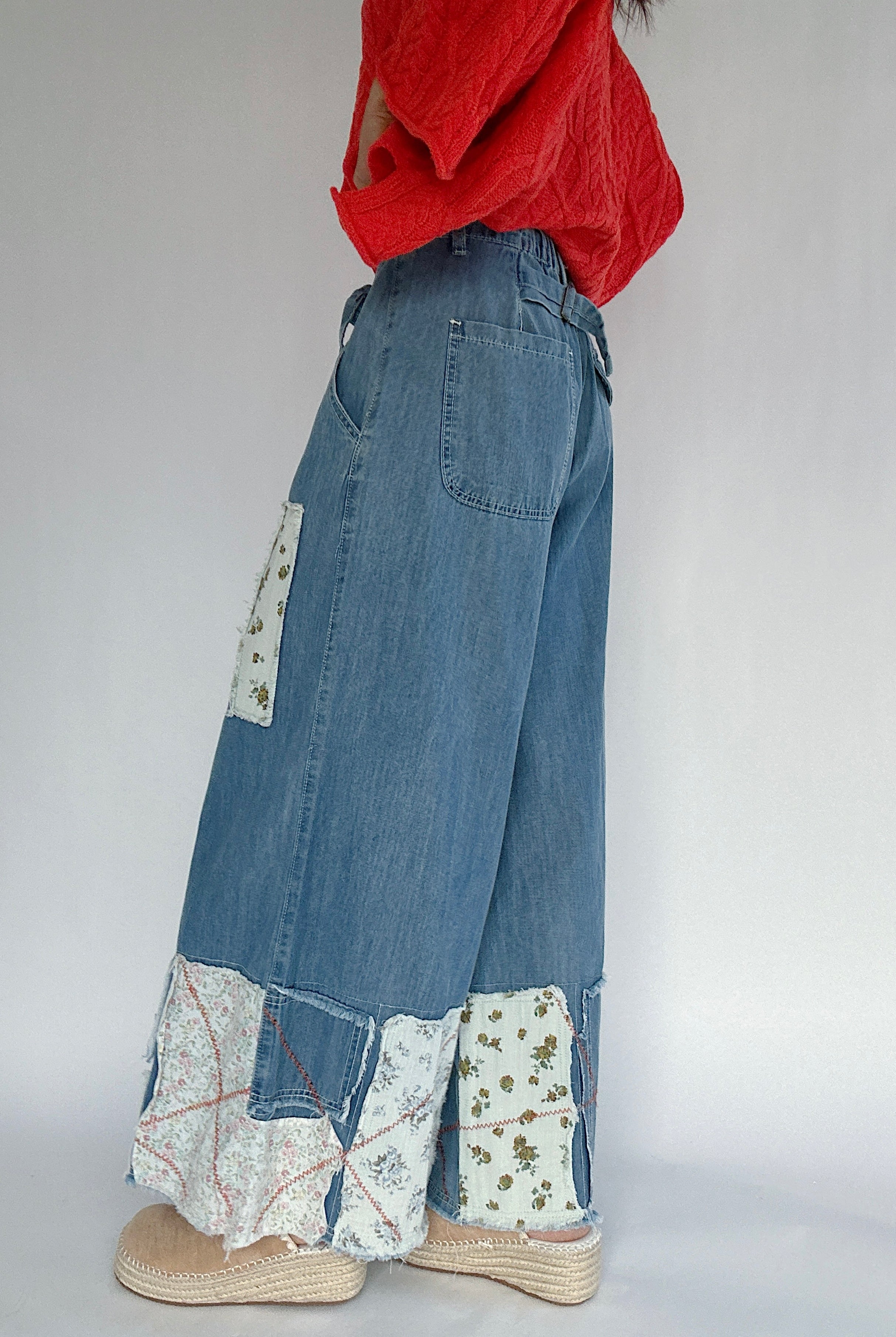 Person wearing blue denim pants with floral print patches on a plain background