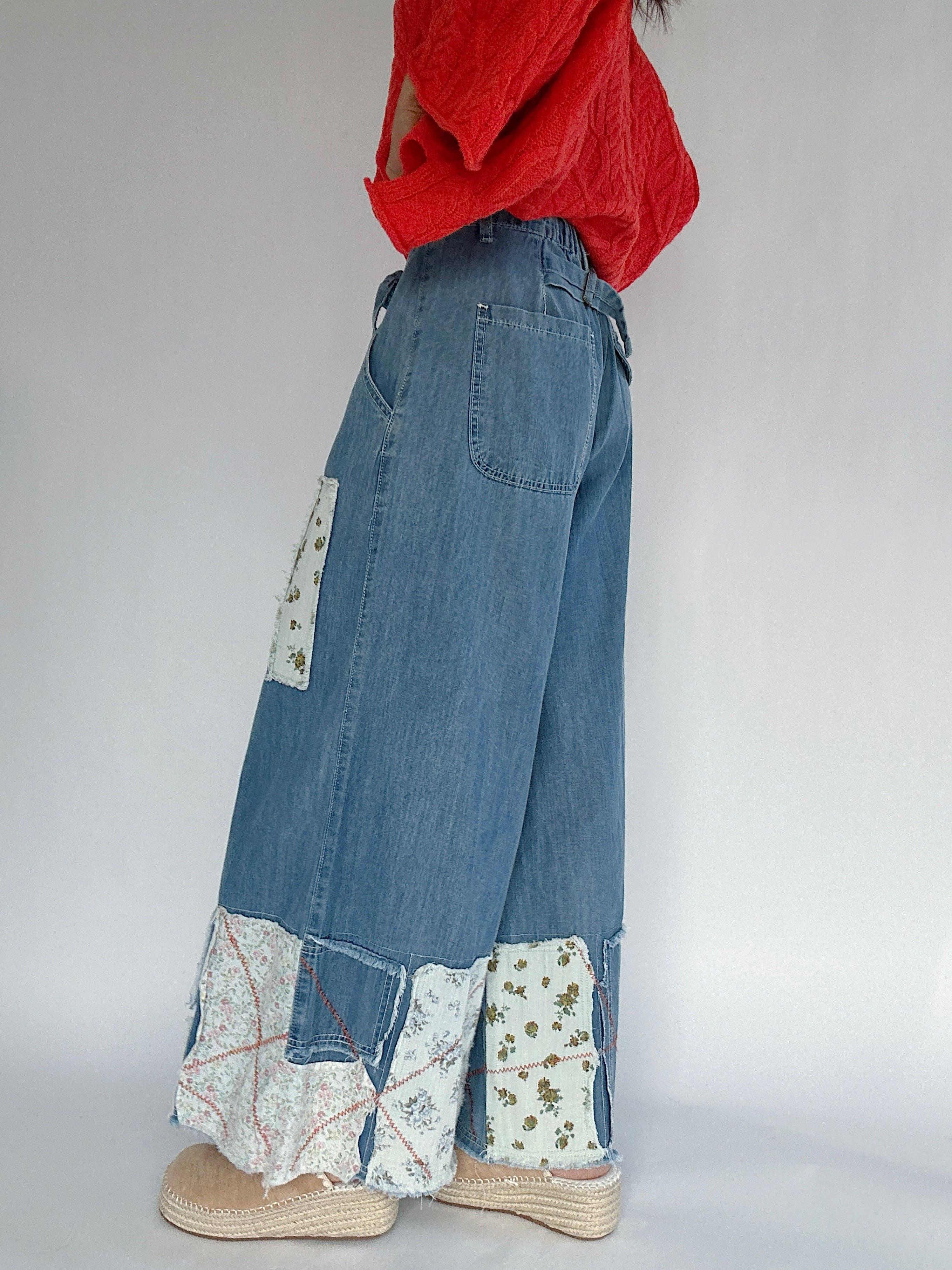 Person wearing blue denim pants with floral print patches on a plain background