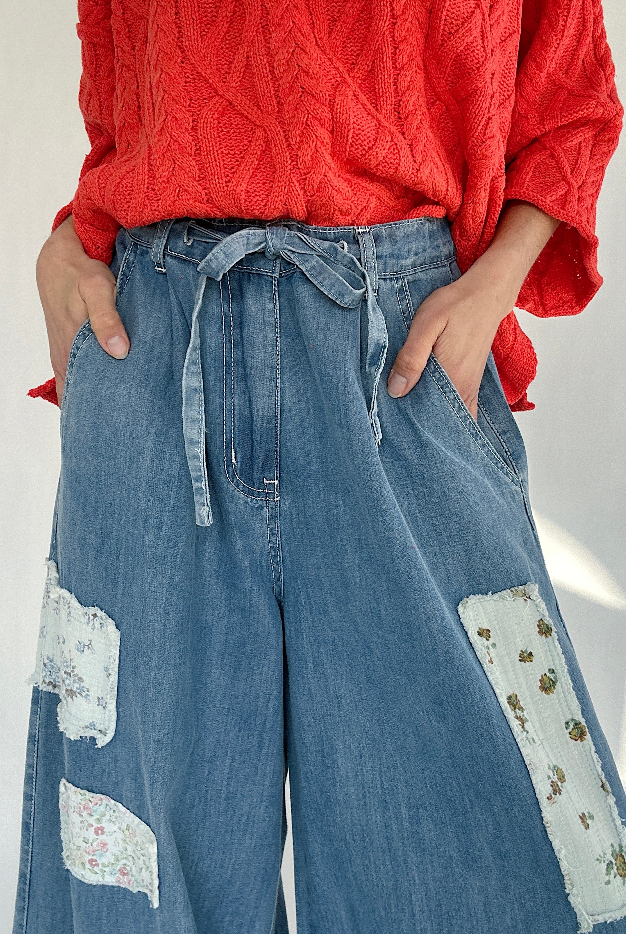 Person wearing a coral sweater and blue jeans with floral patches on a white background to show drawstring waist and side pockets