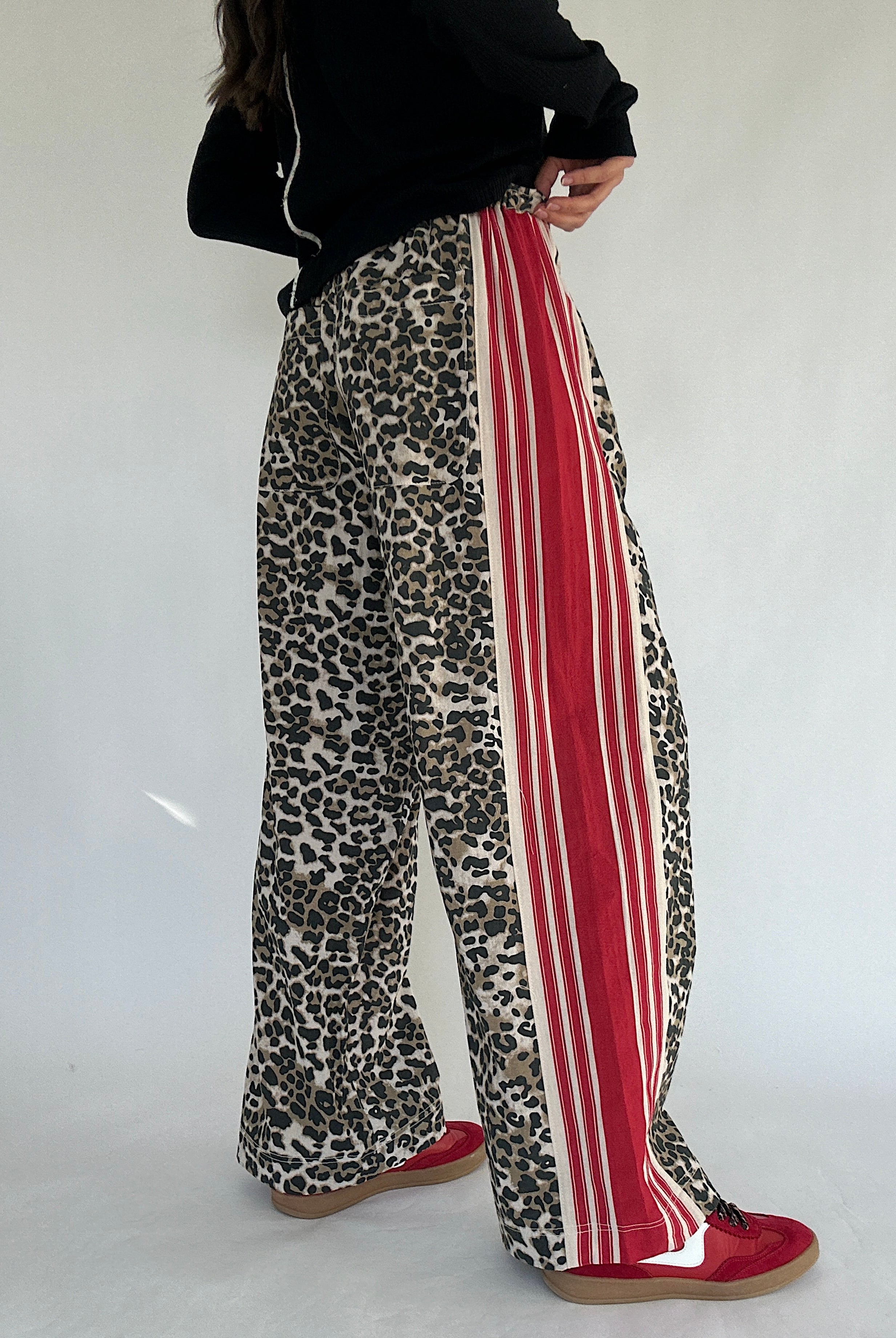 Leopard print pants with red stripes worn by a person on a white background