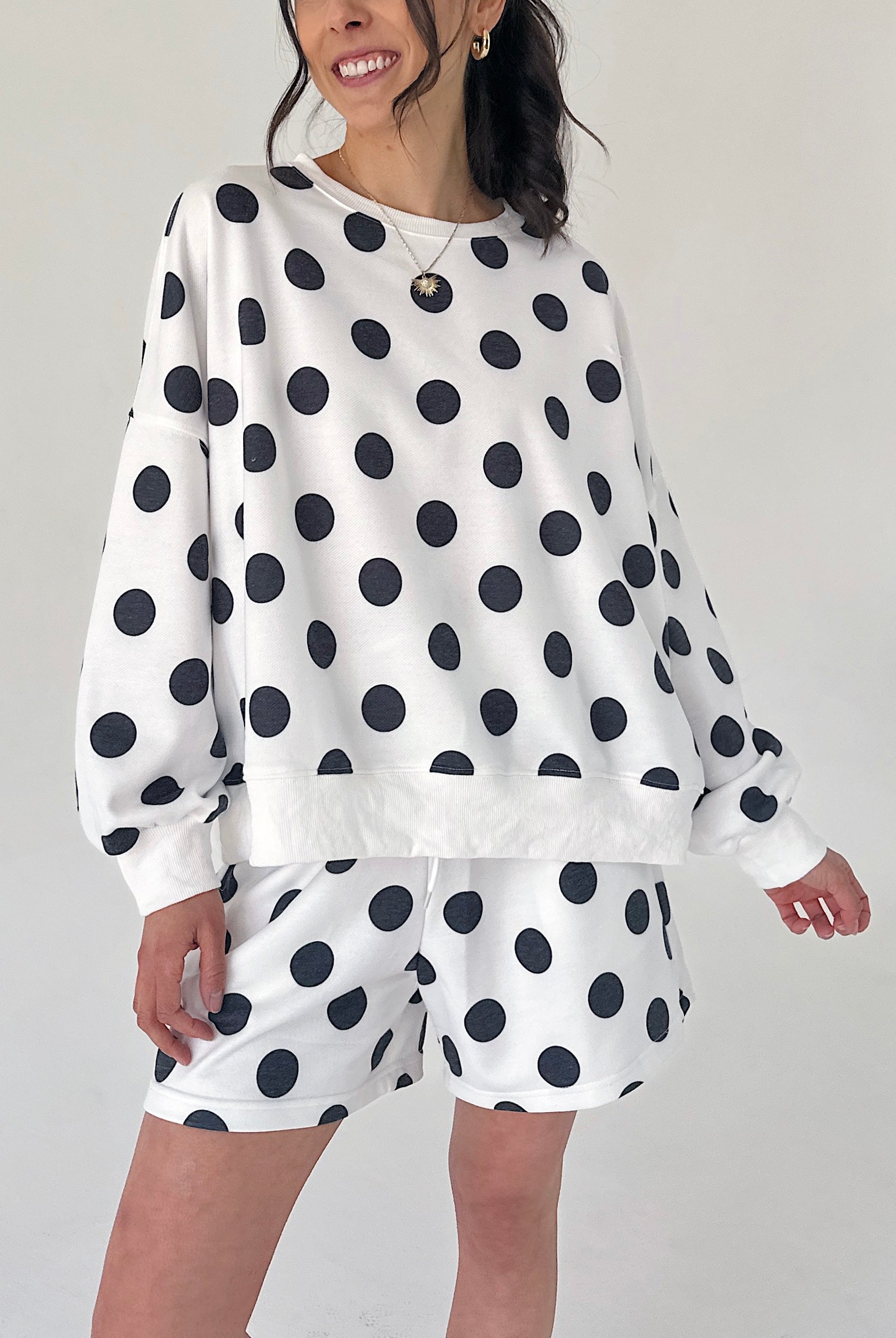 Person wearing a white sweatshirt with black polka dots and matching shorts on a plain background