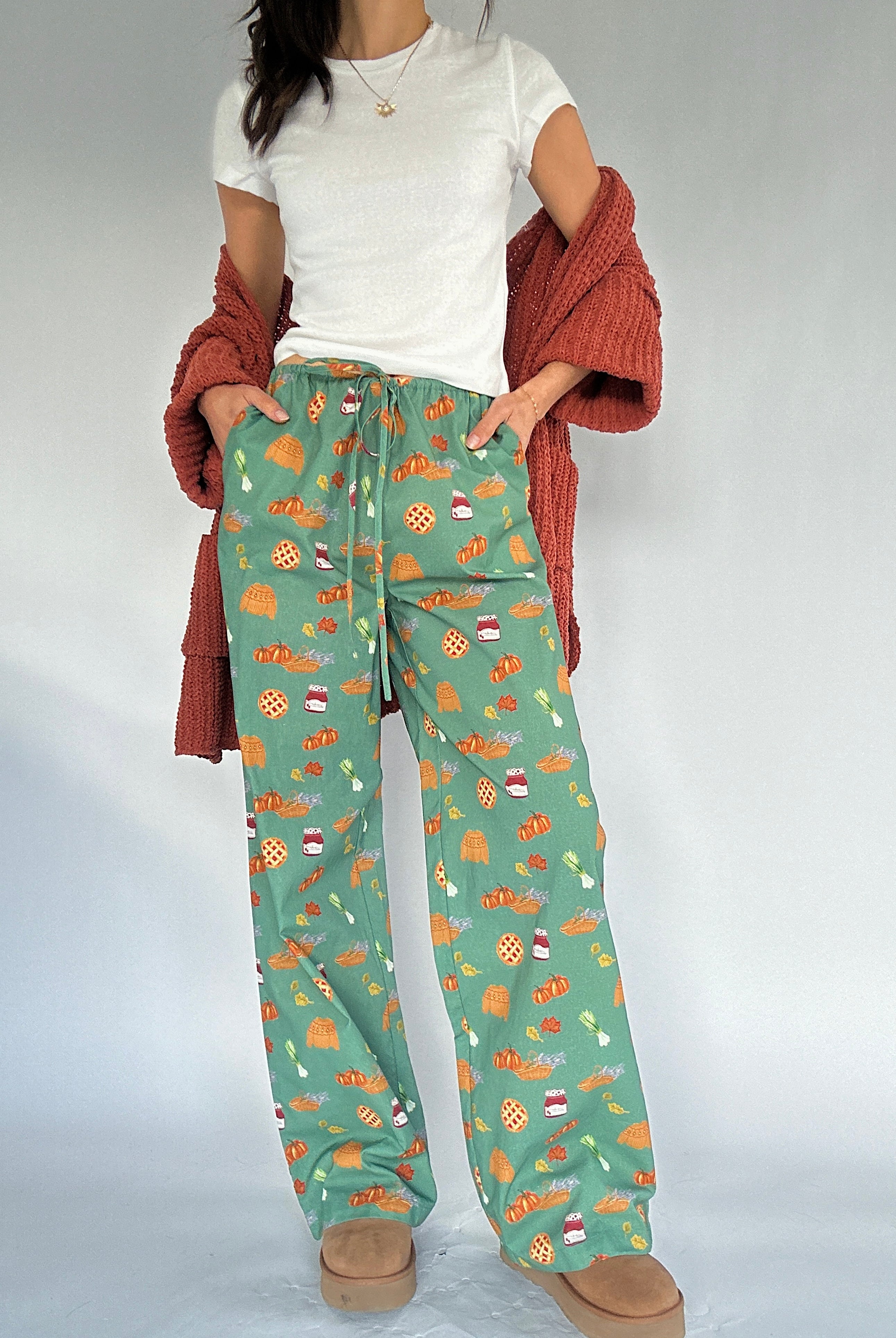 Person wearing green fall patterned pants with a white shirt and rust cardigan sweater on a light gray background