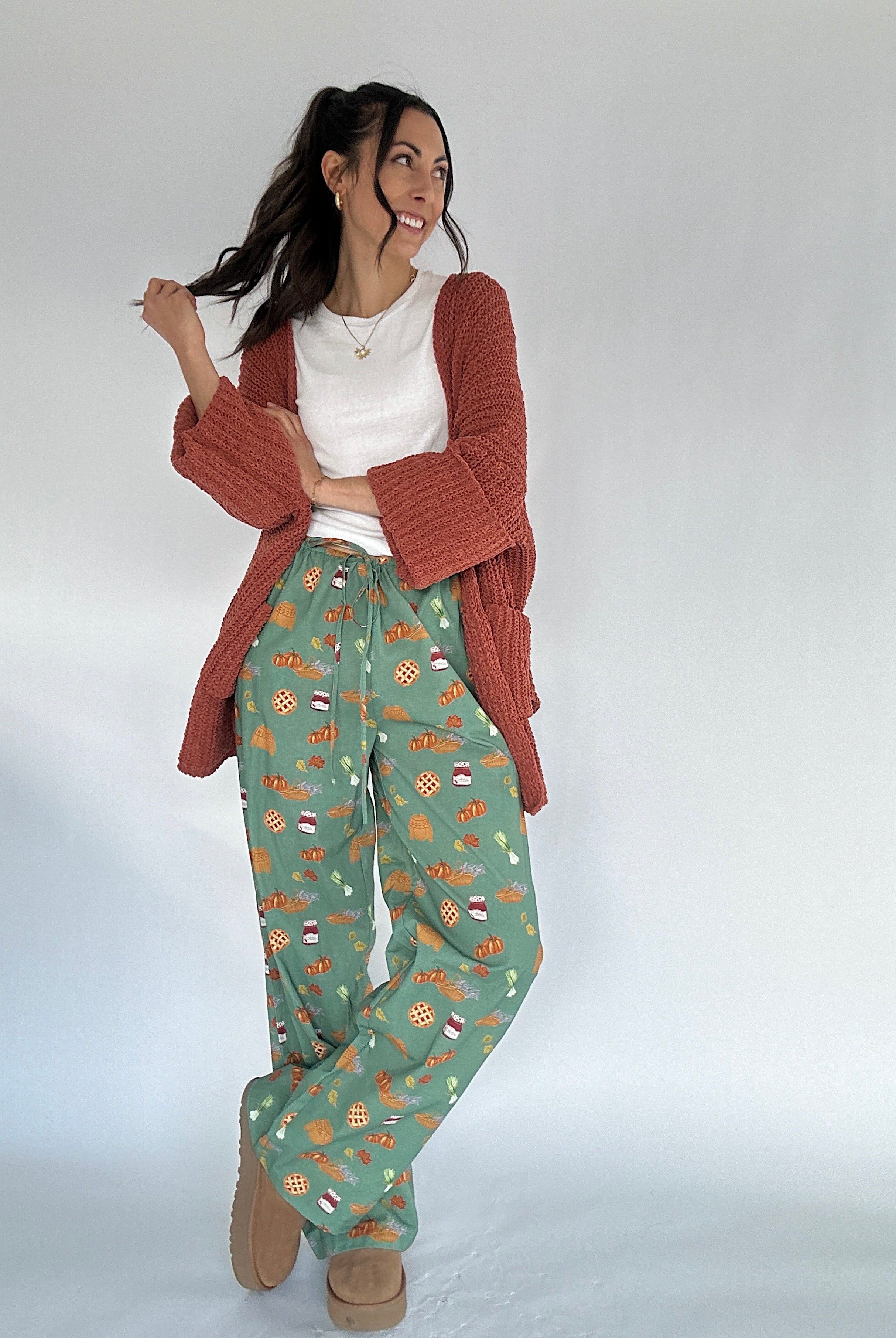 Woman wearing fall patterned green pants and rust cardigan on a white background