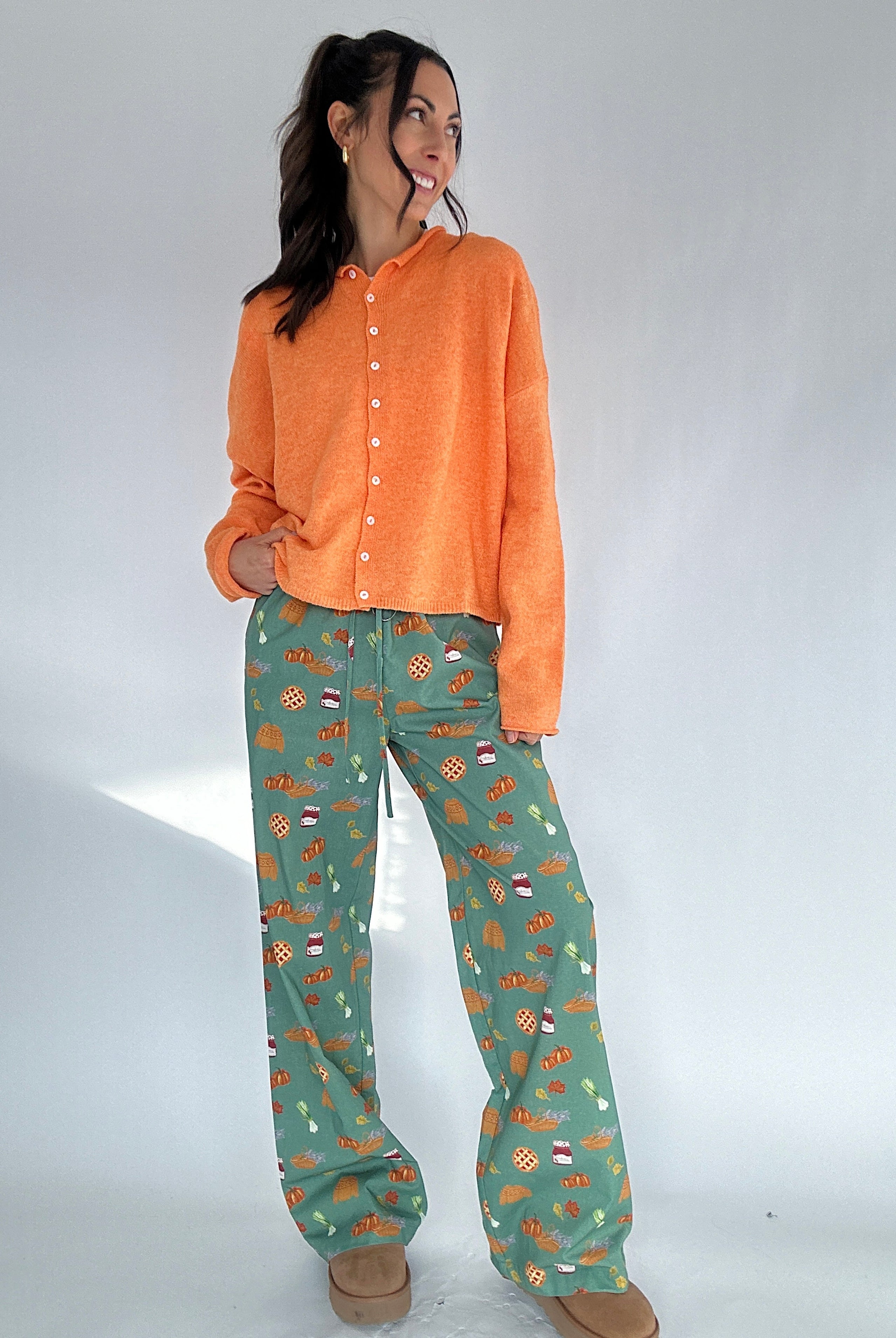 Woman wearing an orange cardigan and green fall inspired patterned pants on a white background