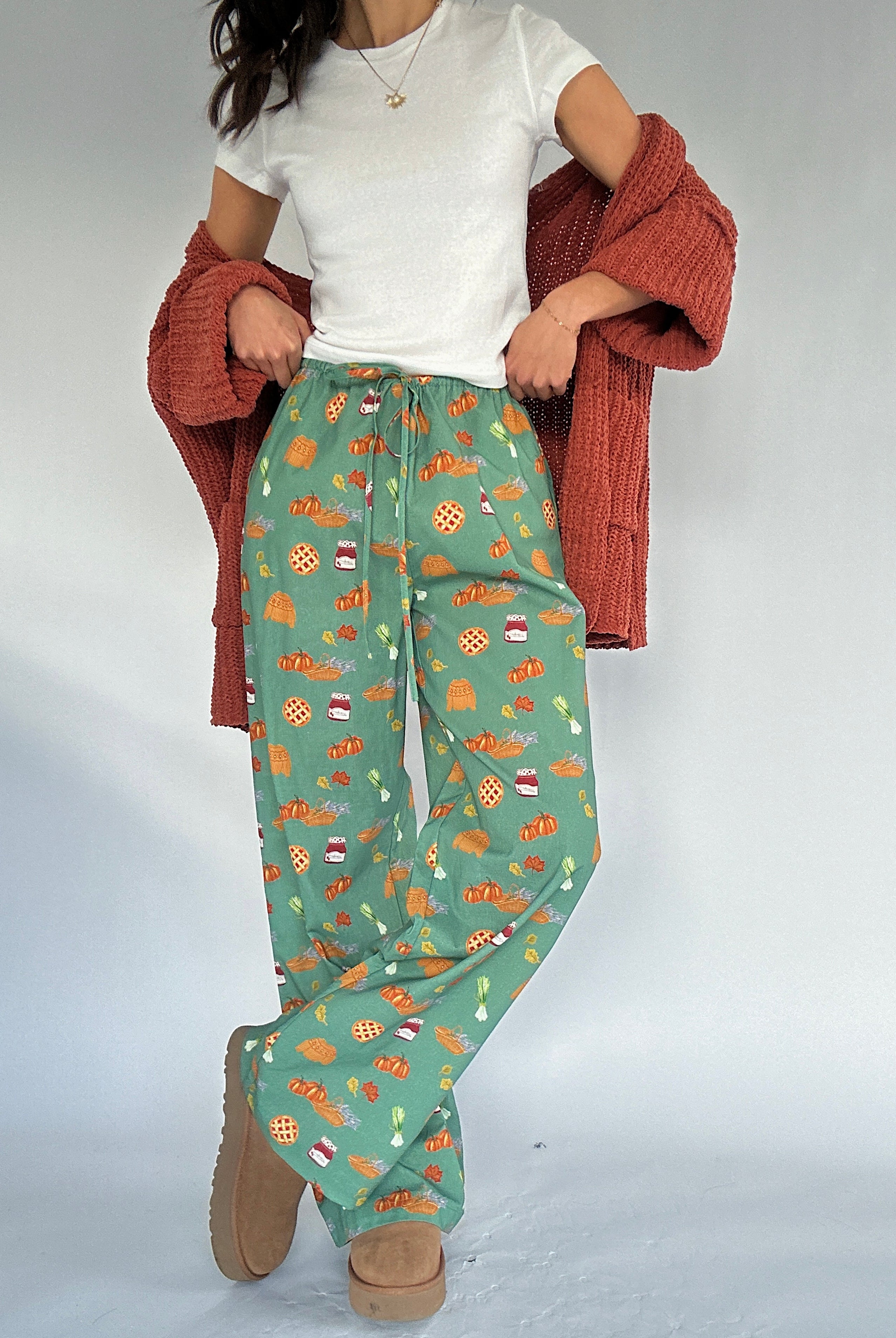 Person wearing green fall patterned pants with a white top and rust cardigan on a plain background