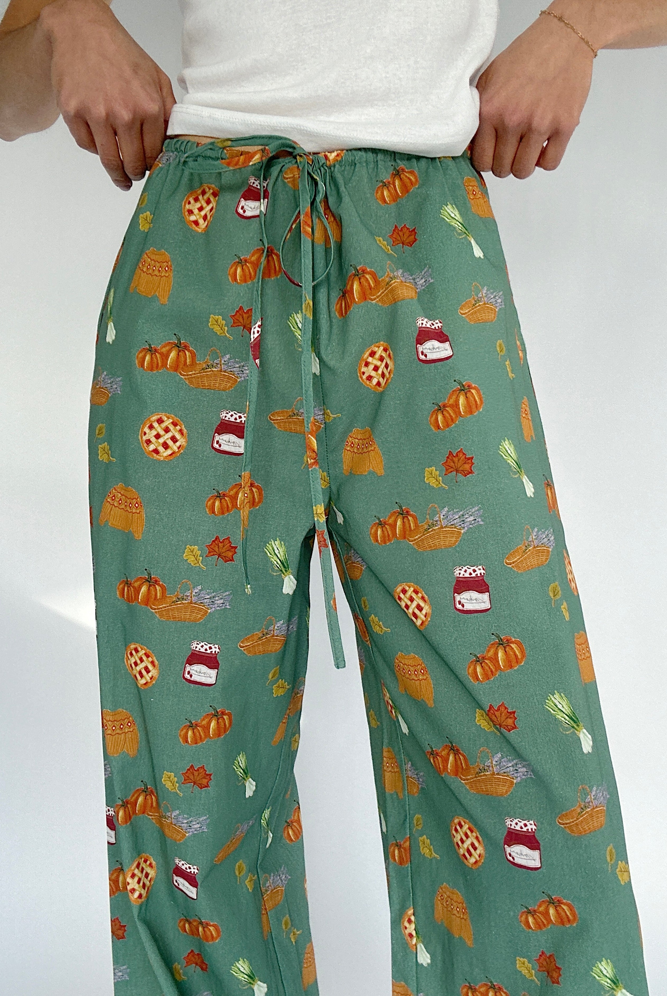 Green pants with autumn-themed pattern on a white background showing drawstring waist