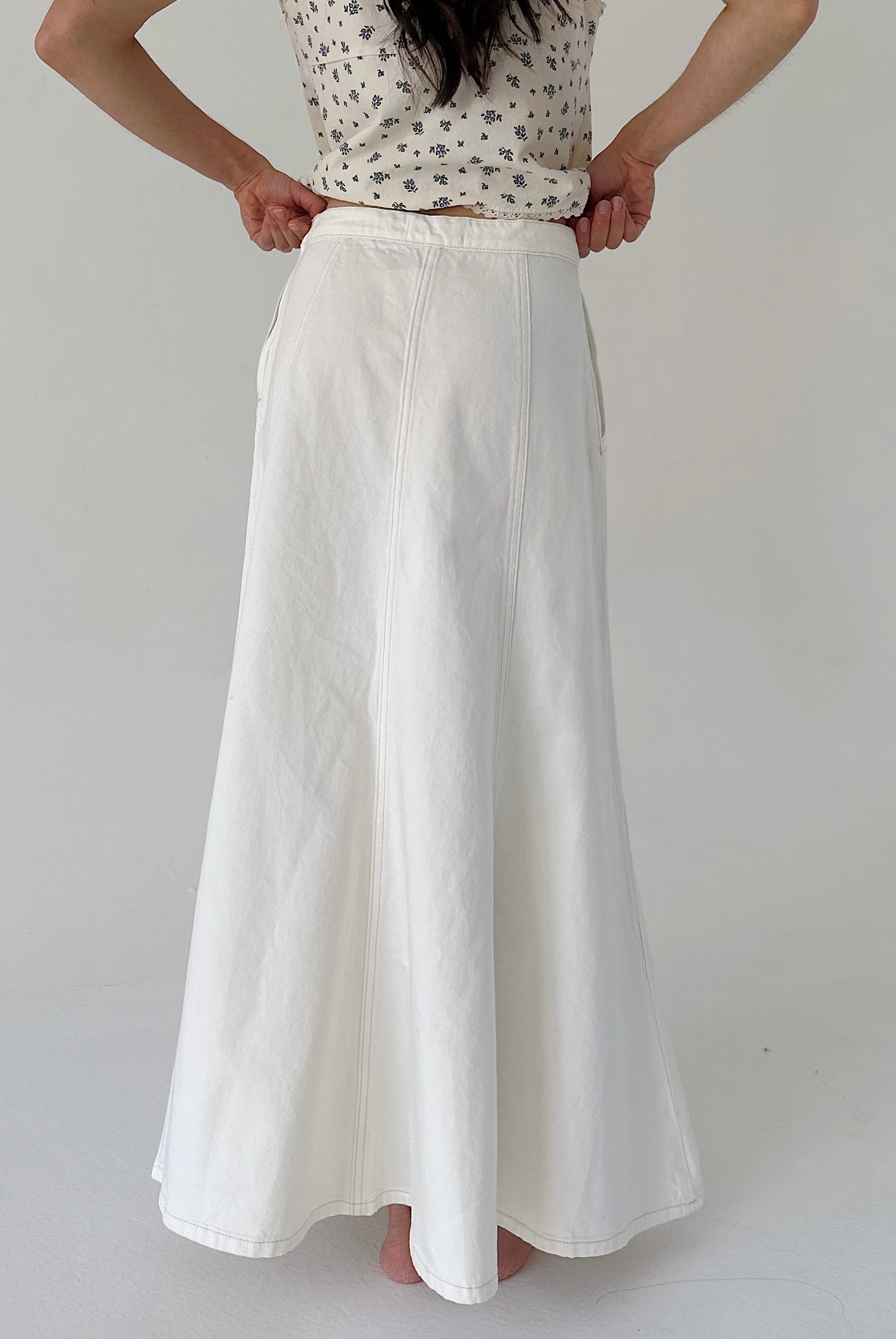 Person wearing a white skirt and patterned top on a plain background