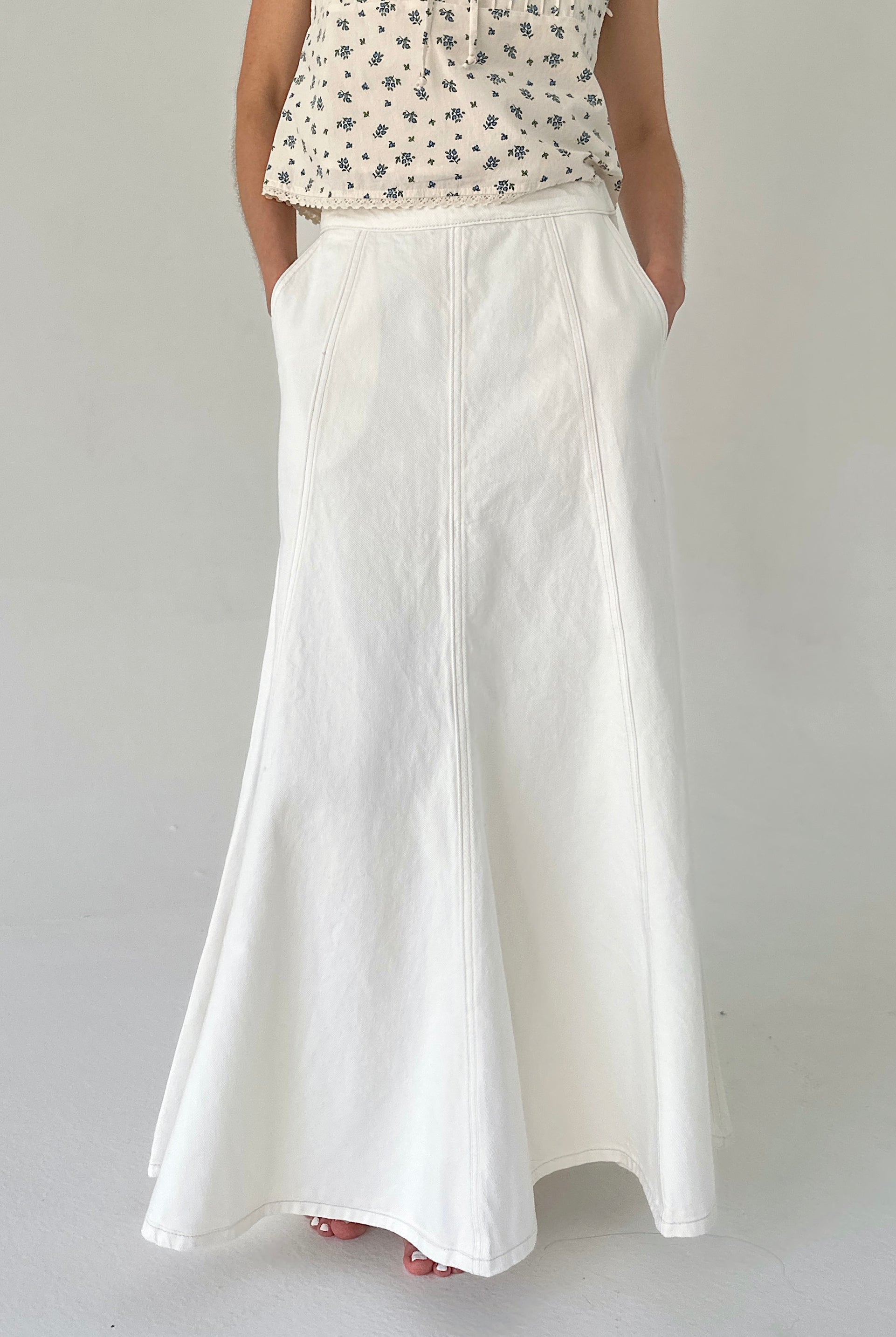 Person wearing a white skirt and patterned top on a plain background