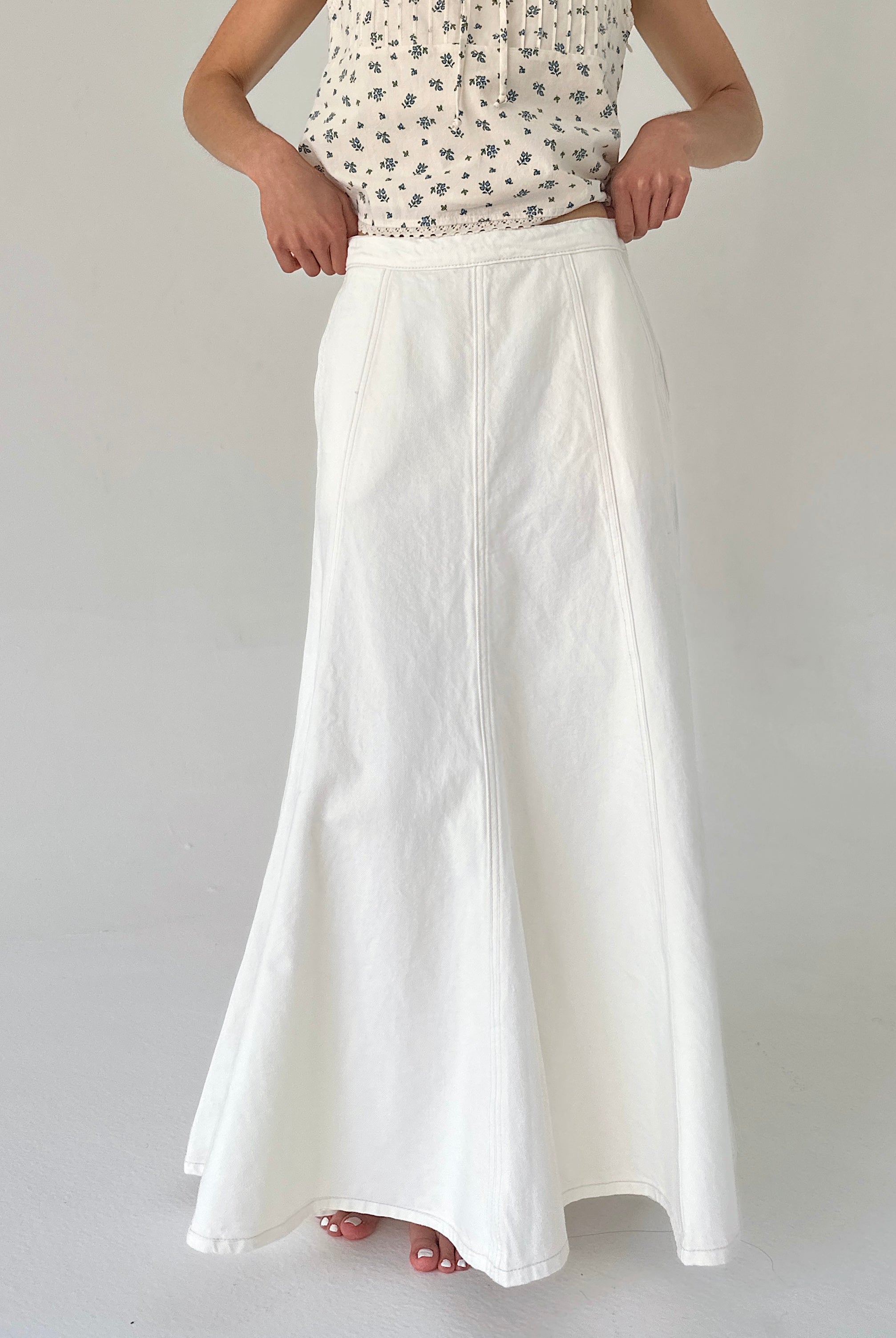 Person wearing a white skirt and patterned top on a plain background