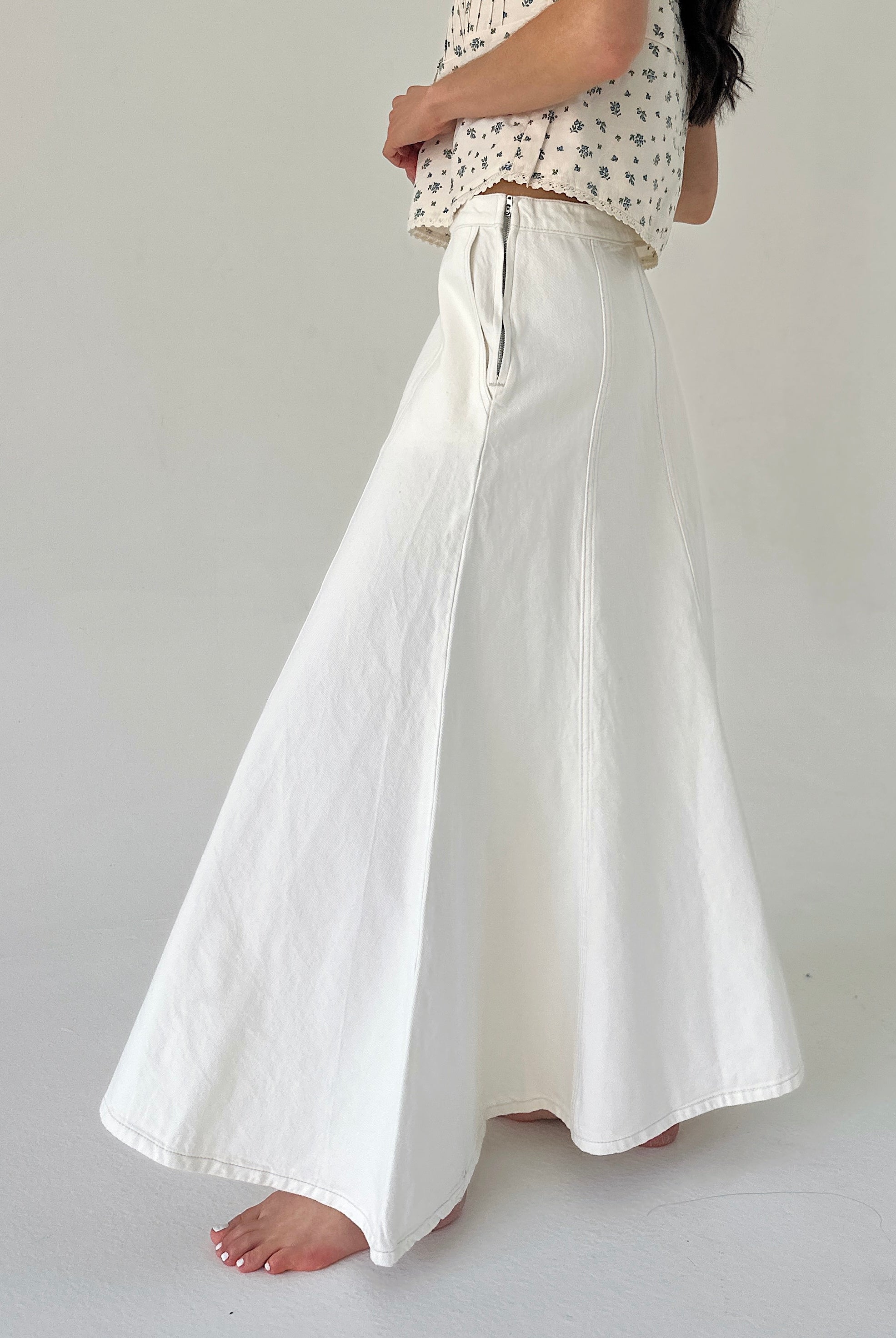 Person wearing white denim maxi skirt on a plain background showing side zipper