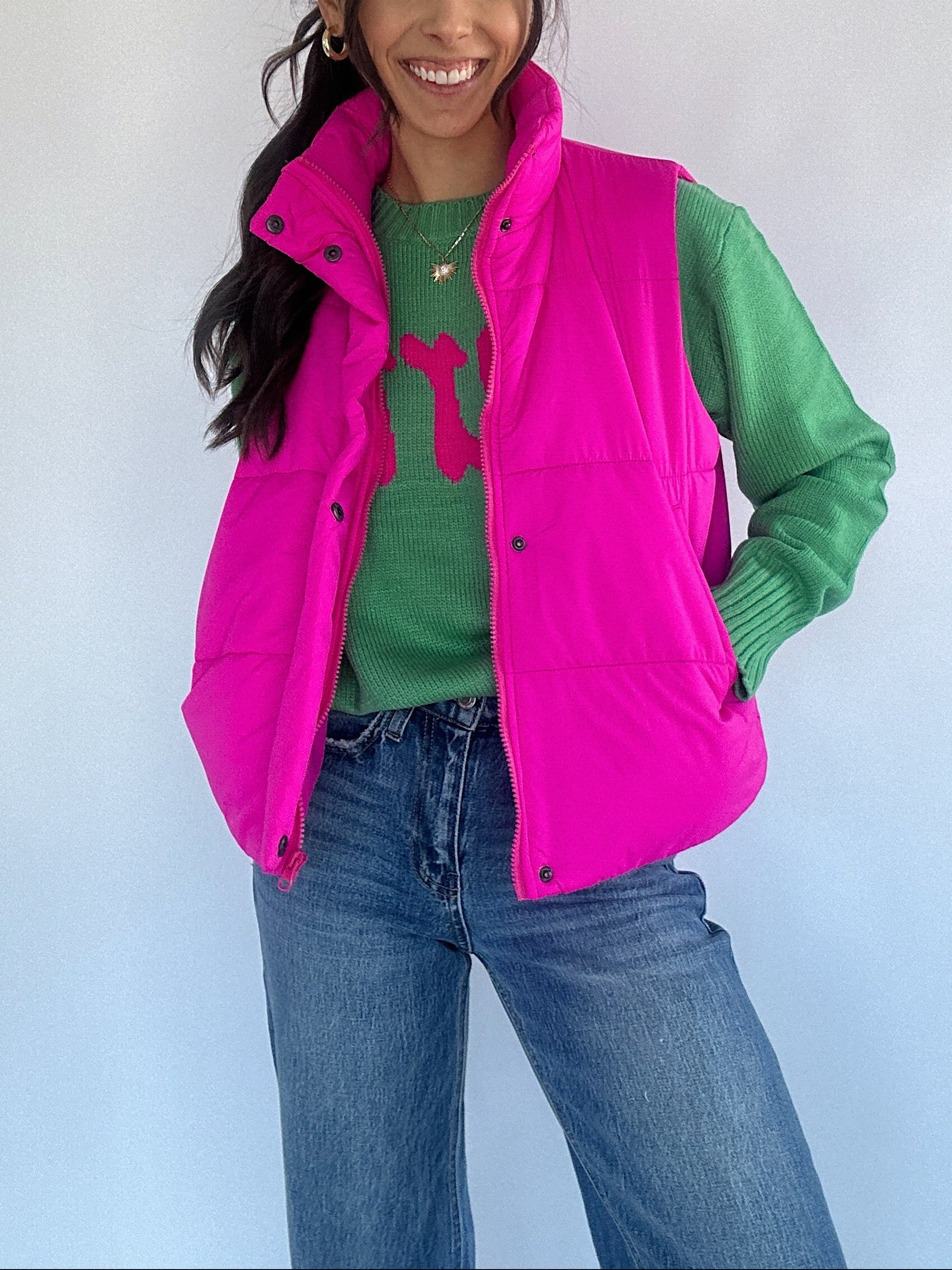 Woman wearing a bright pink vest over a green sweater with a plain background
