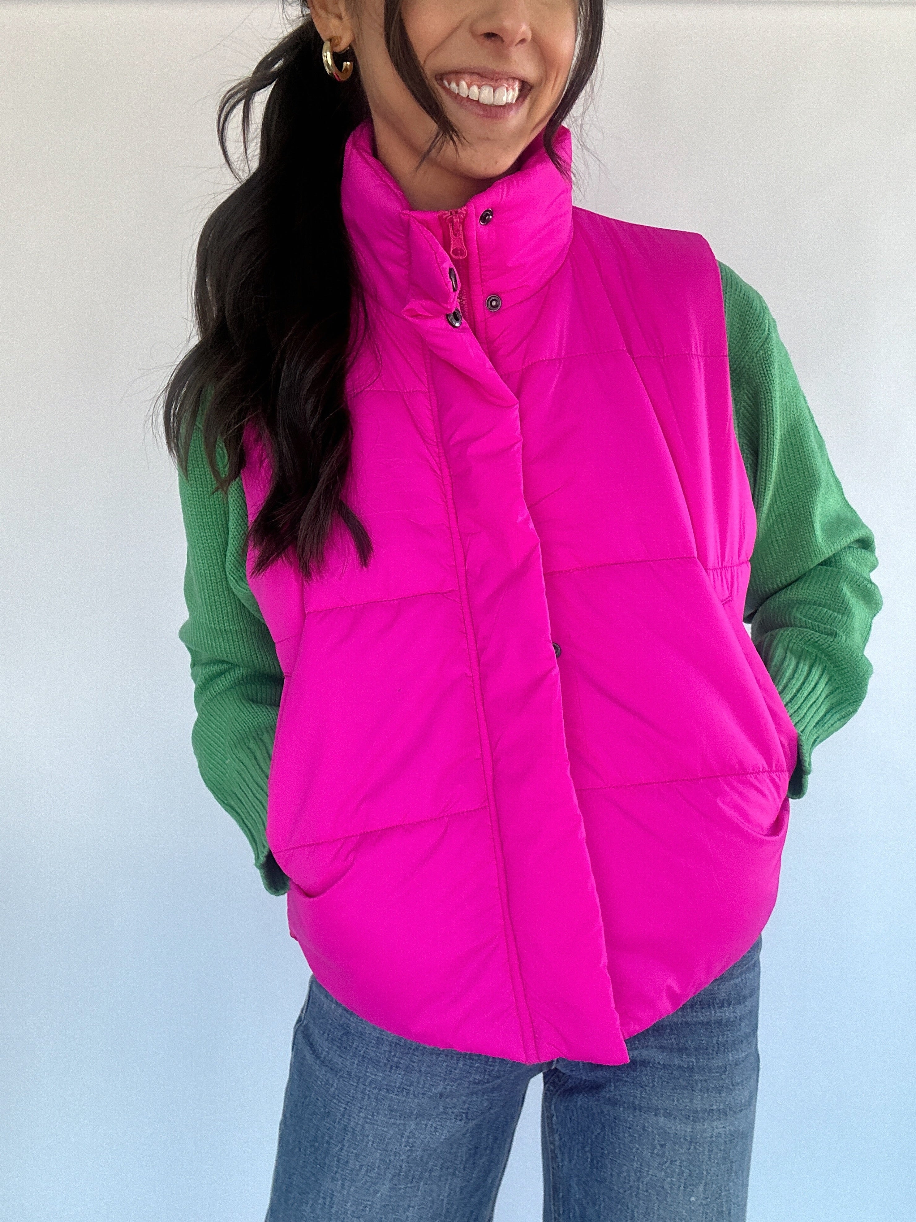 Hot pink puffer vest buttoned over a green sweater