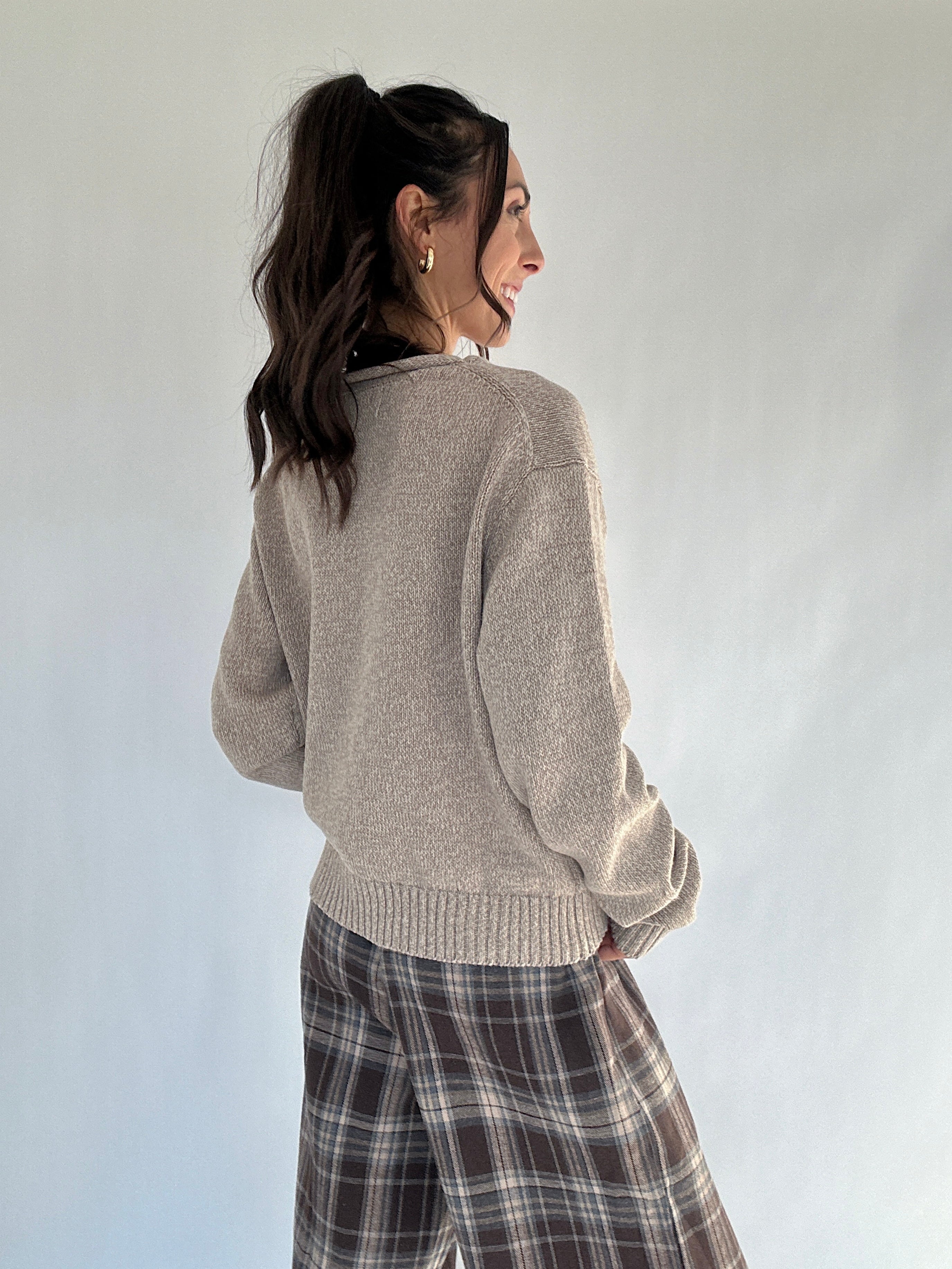 Woman wearing a beige sweater and plaid pants against a white background from back