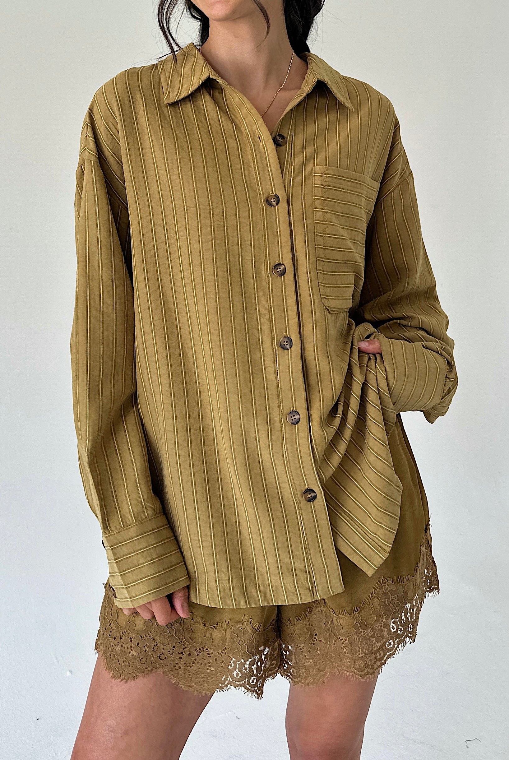 A person wearing an oversized long-sleeve button-front shirt in a warm olive-brown corduroy-like fabric, paired with matching lace-trim shorts, against a plain light background.