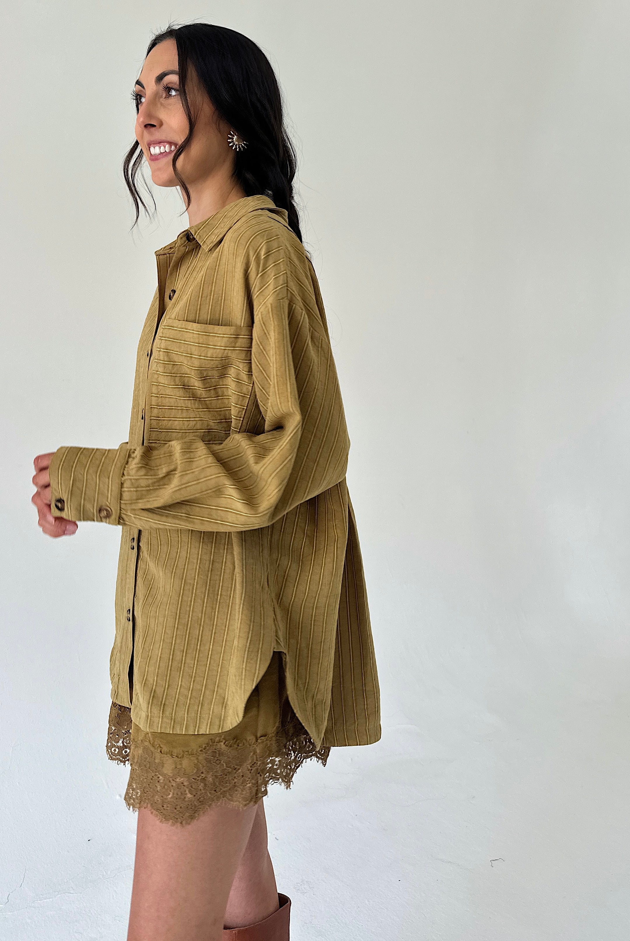 A woman wearing an oversized mustard yellow corduroy button-up shirt with a lace hem, posed against a plain off-white studio background.