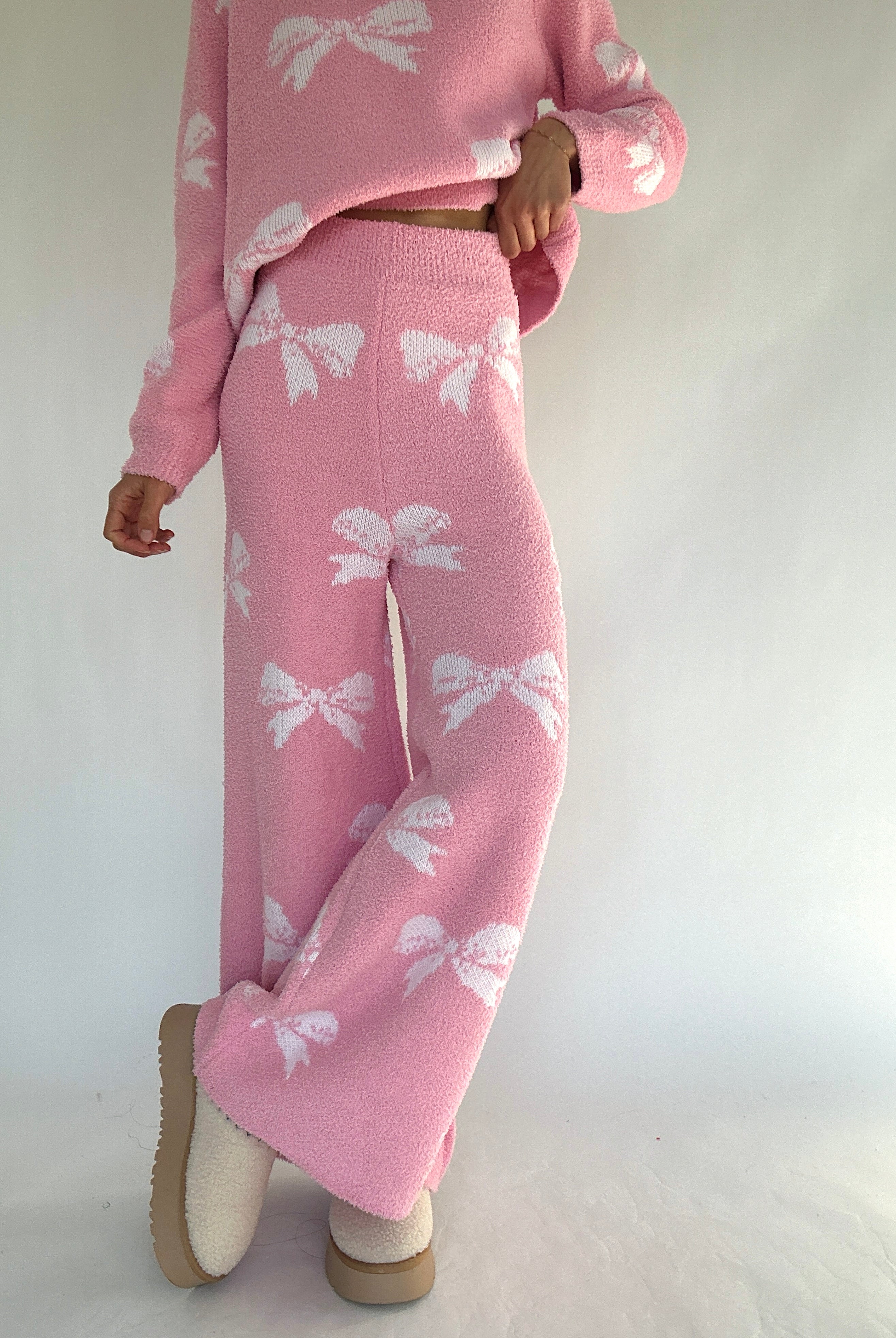 Person wearing a pink set with white bow patterns on a plain background showing pants from front