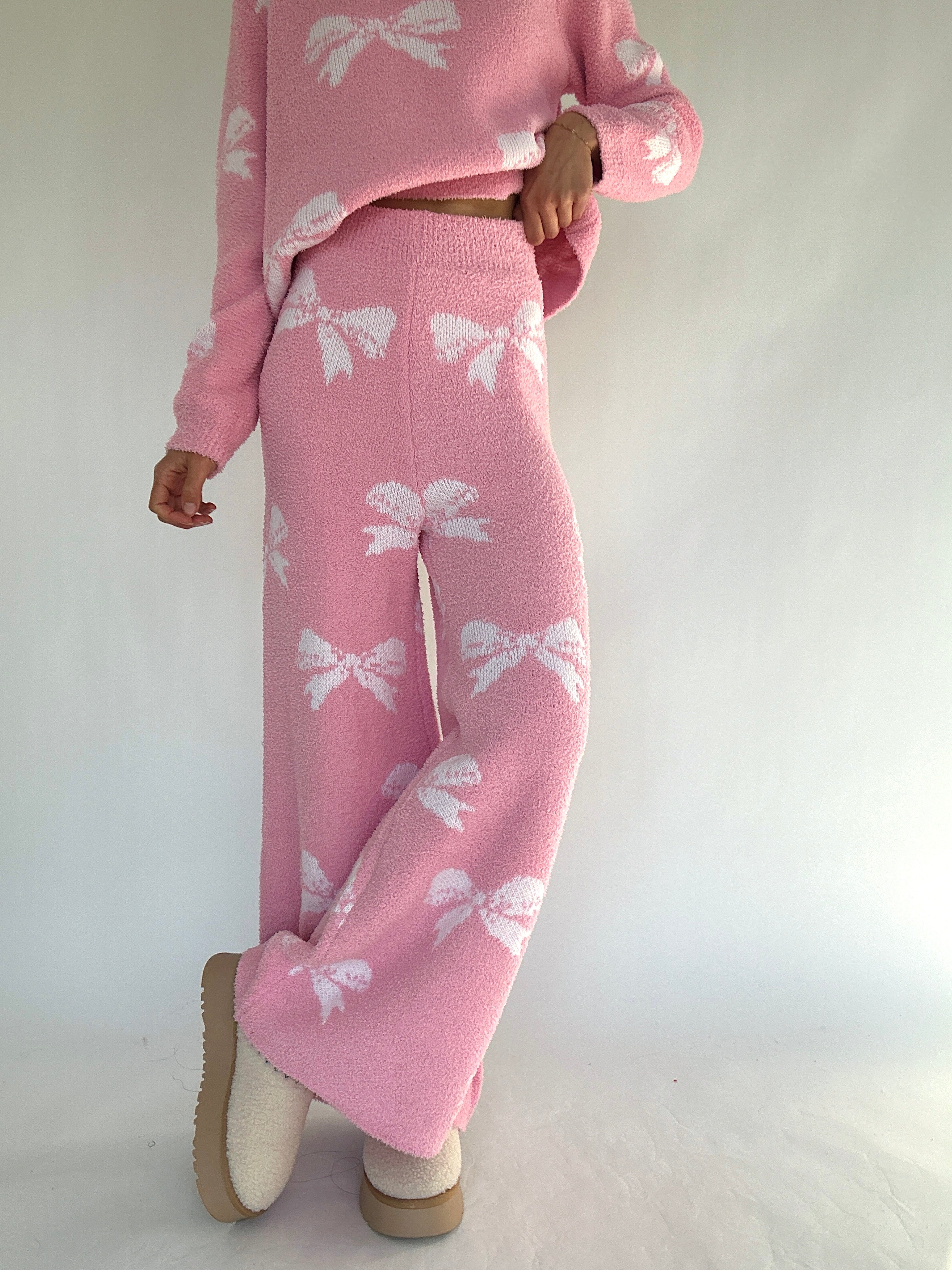 Person wearing a pink set with white bow patterns on a plain background showing pants from front
