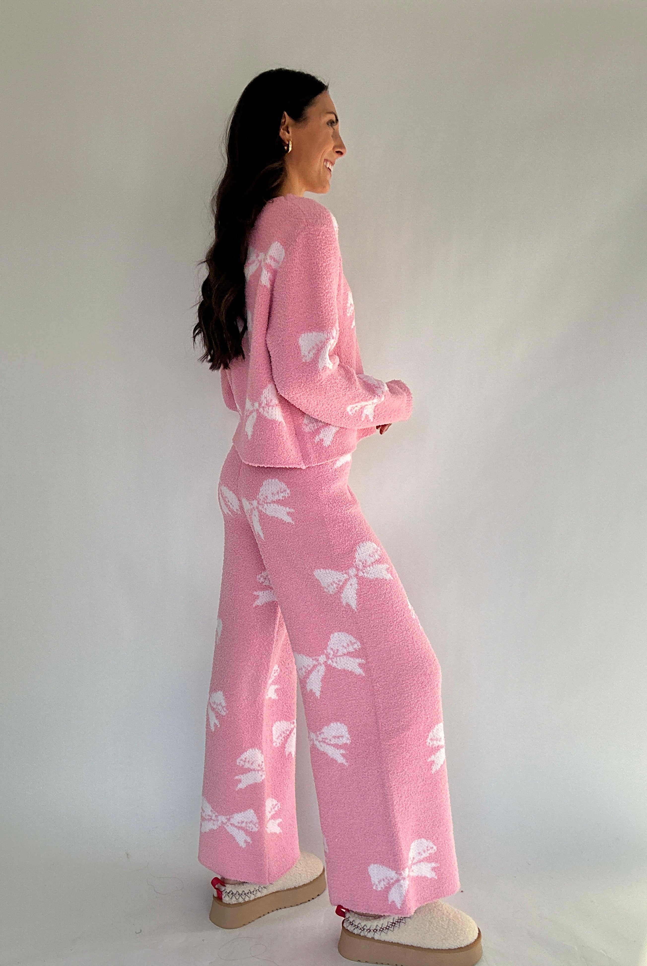 Woman wearing a pink outfit with white bow patterns against a plain background from side
