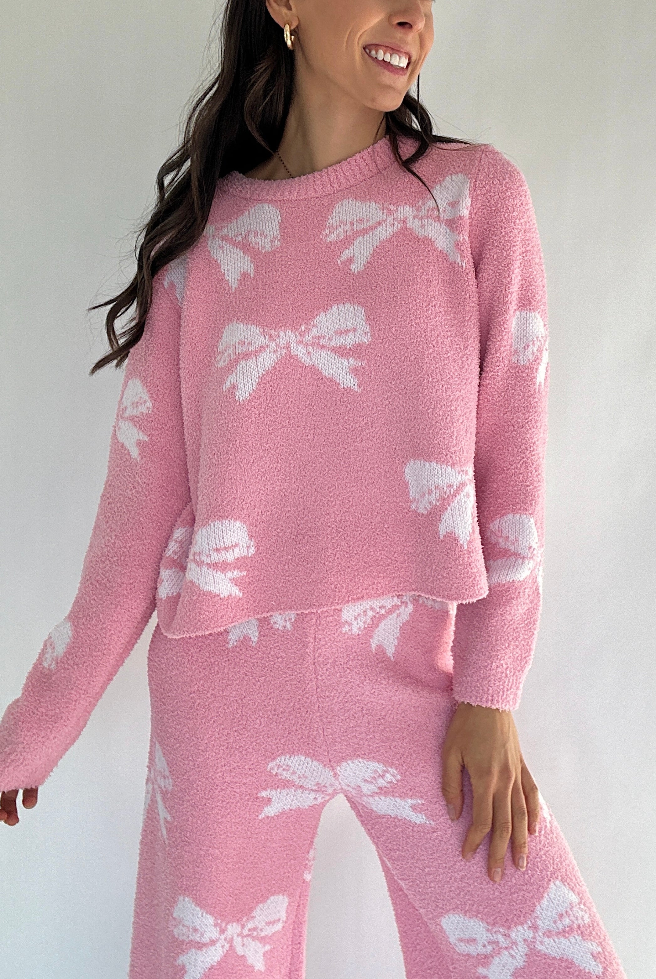 Person wearing a pink sweater with white bow patterns on a plain background with matching pants