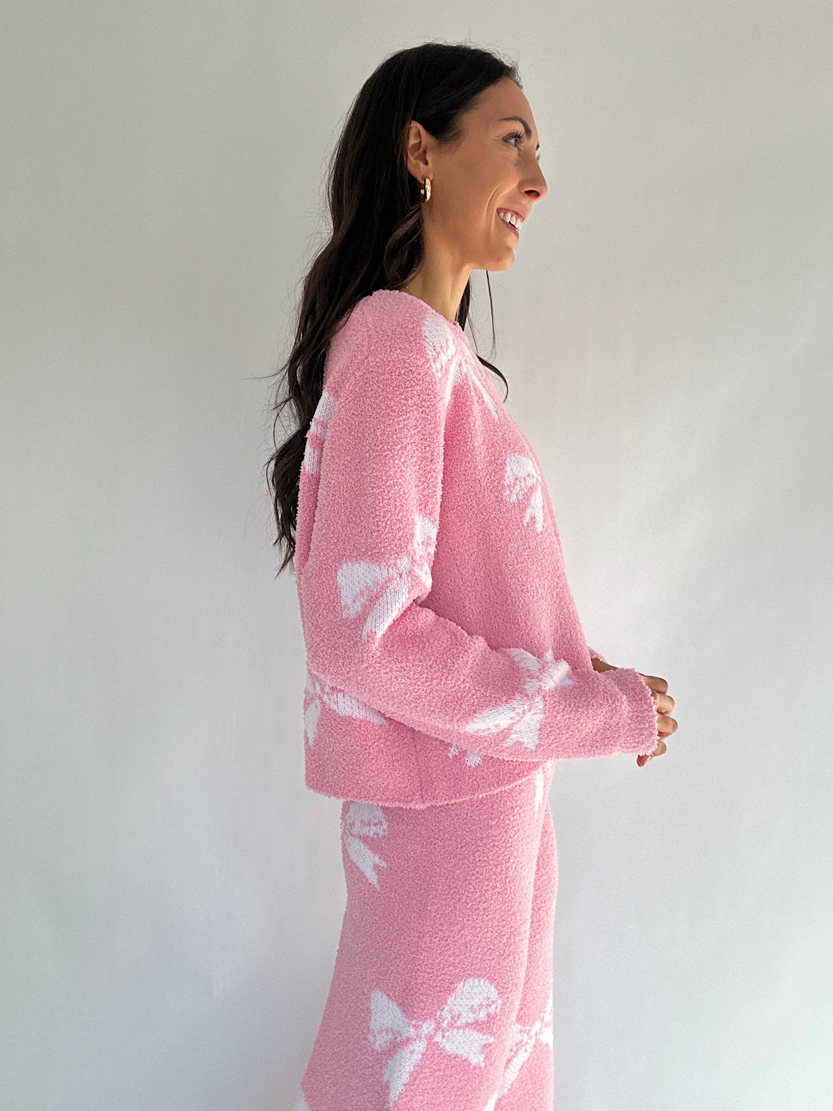 Woman wearing a pink outfit with white bow patterns against a plain background showing top side