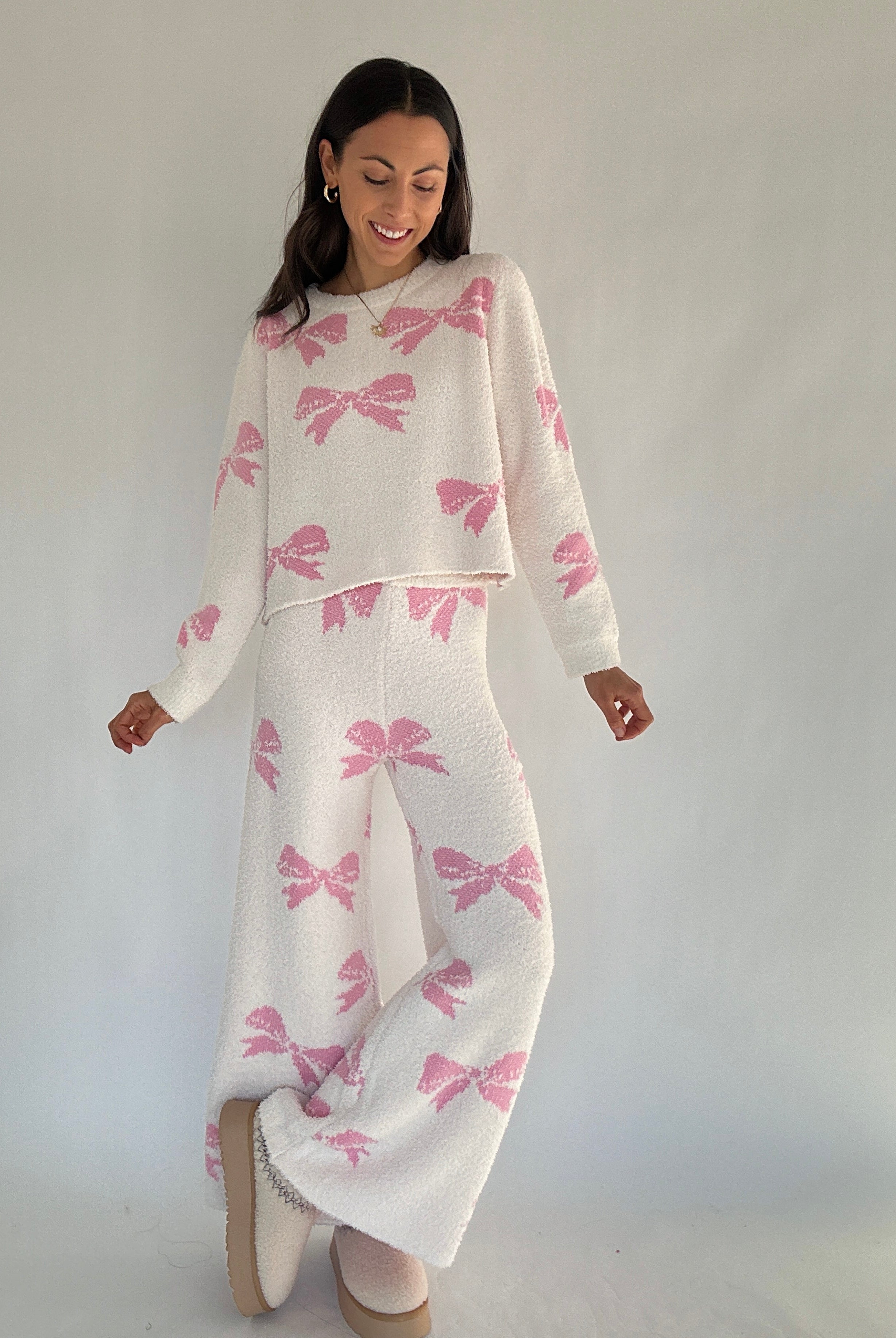 Woman wearing a white matching outfit with pink bows against a plain background