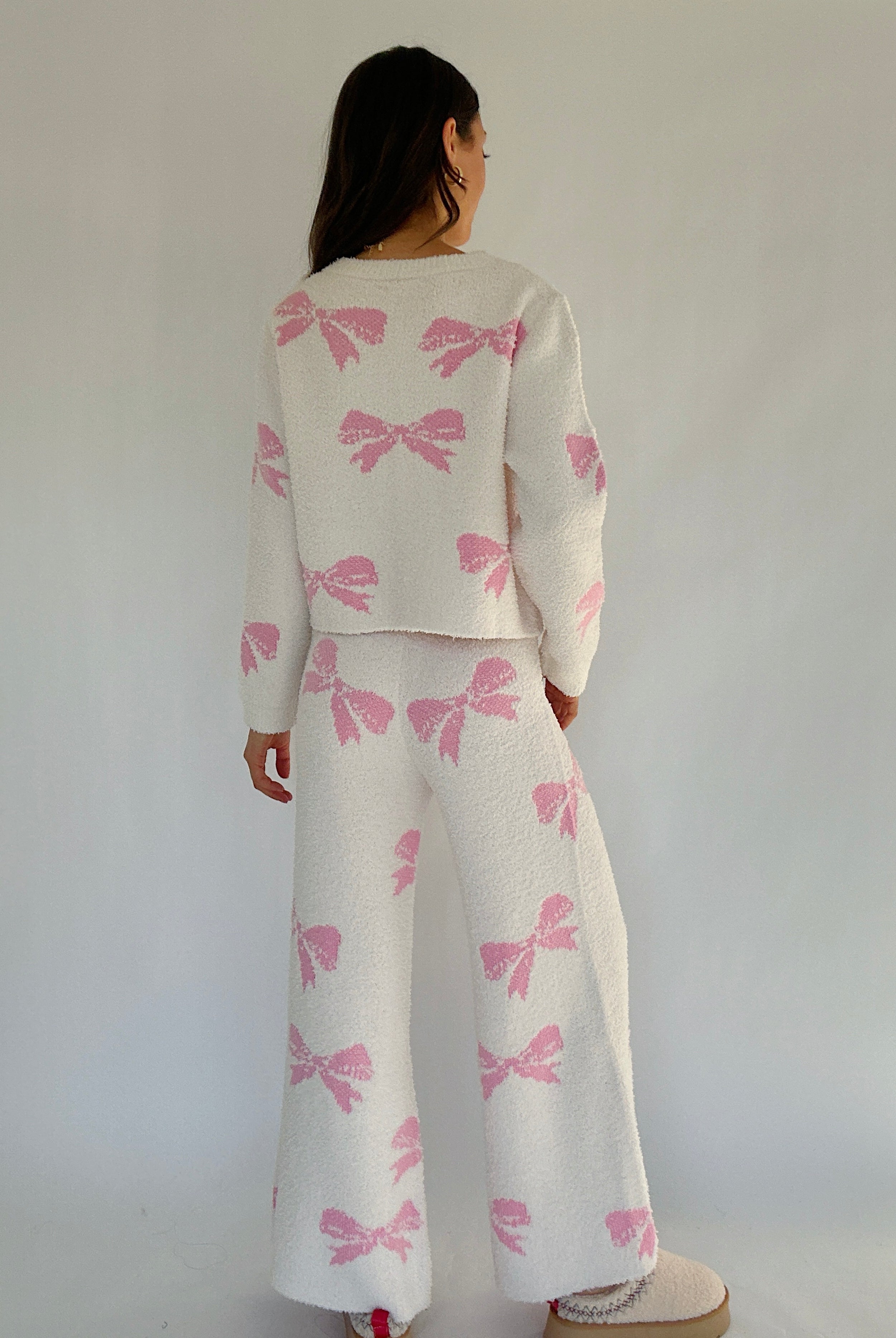 Person wearing a cream outfit with pink bow patterns against a plain background showing back