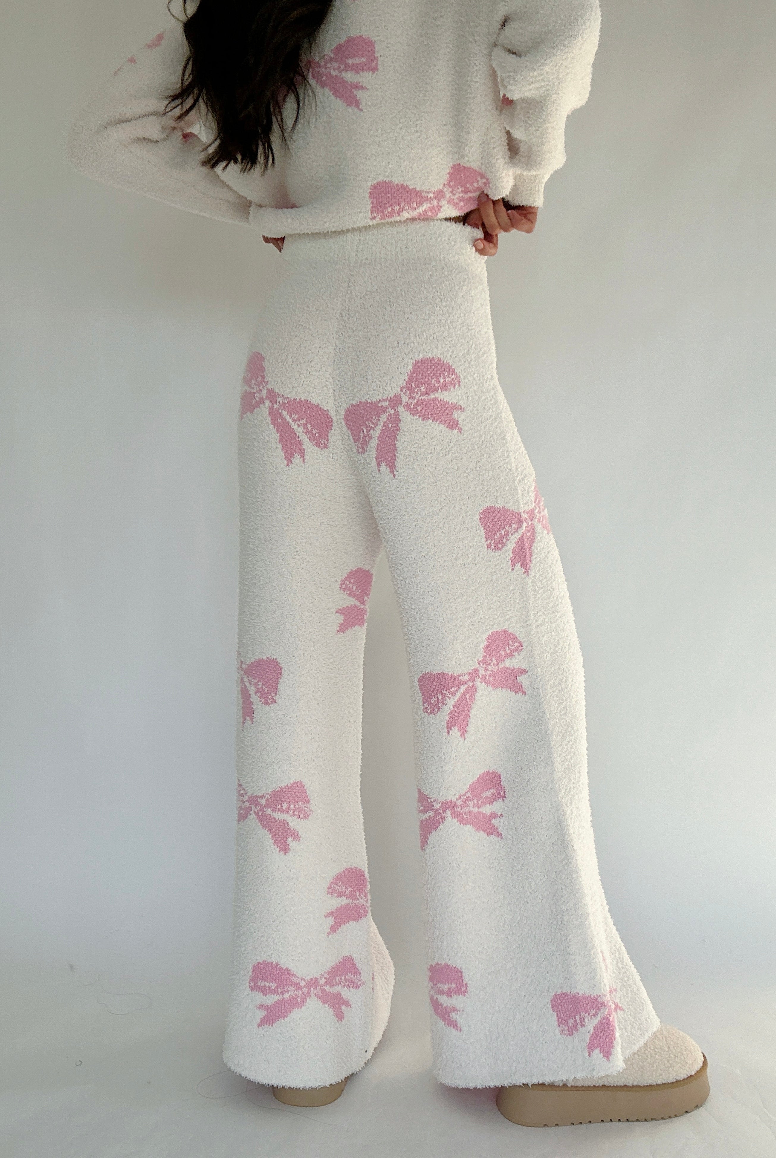 White pants with pink bow pattern worn by a person on a white background showing back of pants