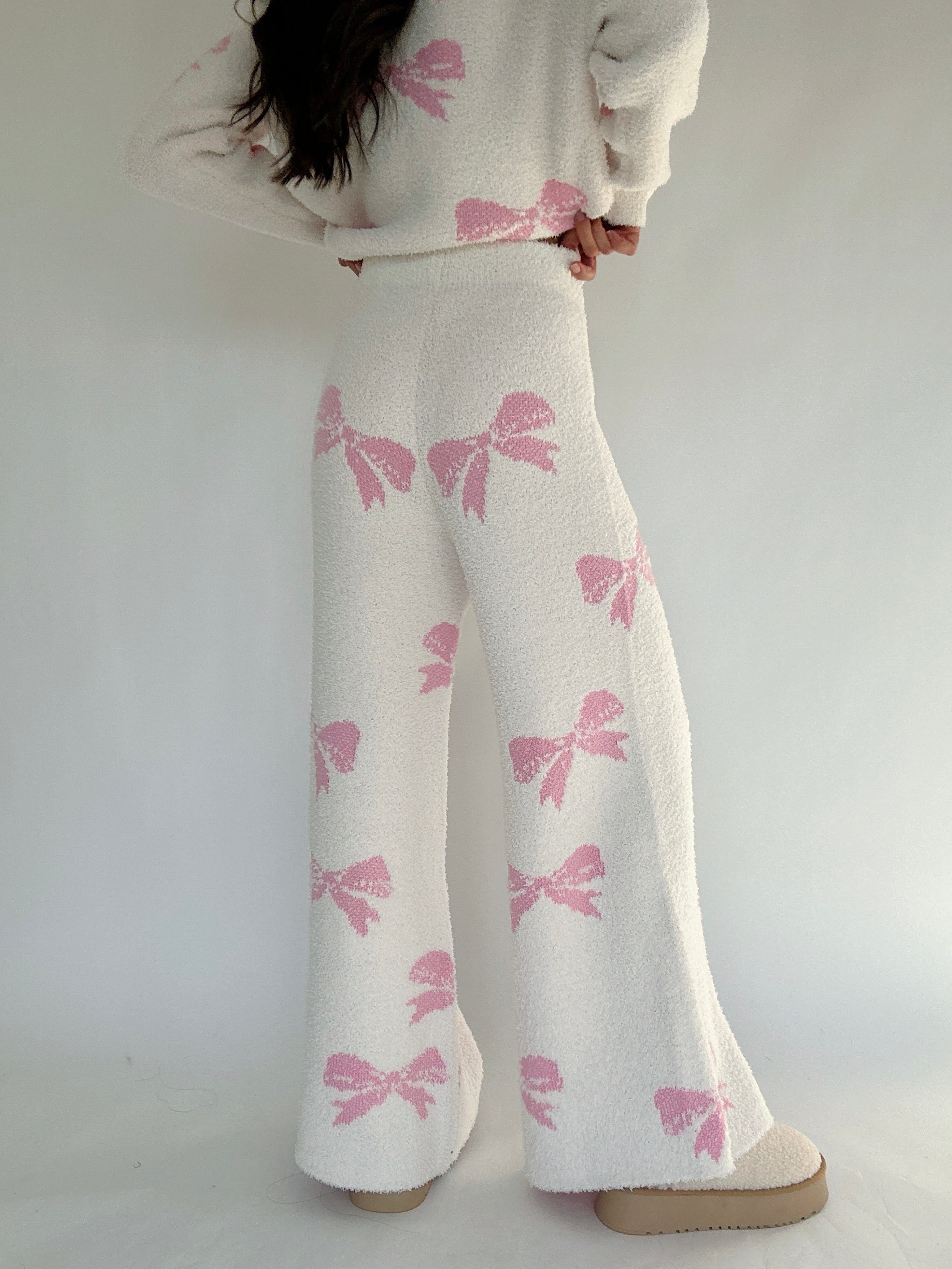 White pants with pink bow pattern worn by a person on a white background showing back of pants